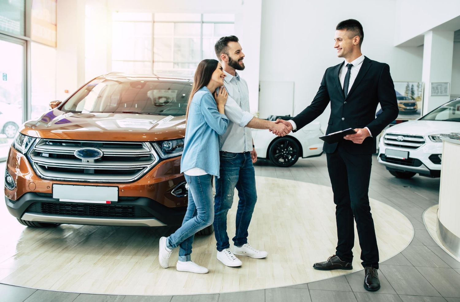 A man and woman are shaking hands with a car dealer in a showroom.