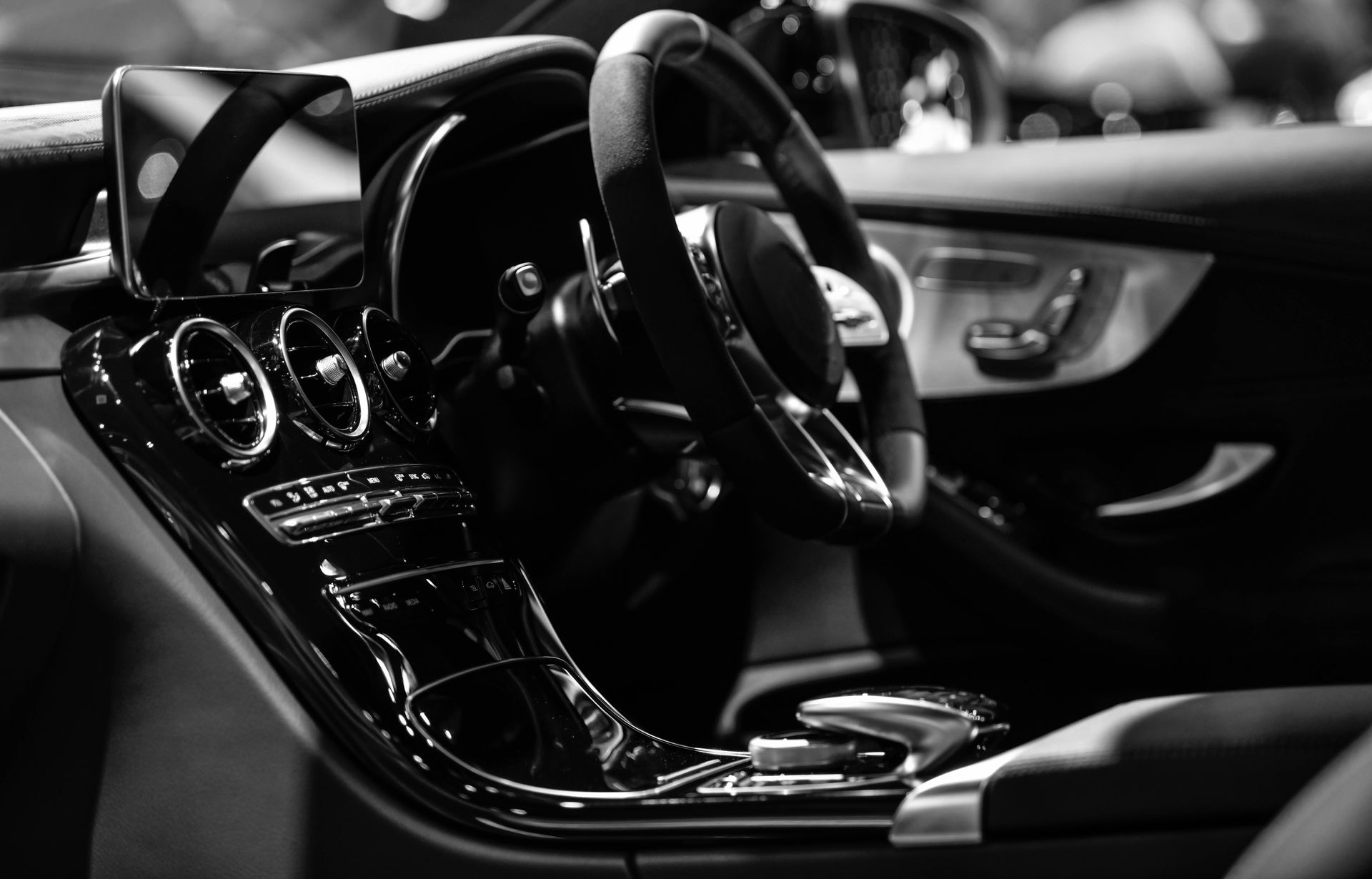 Black and white interior of a luxury car, showing steering wheel, dashboard, and glossy console.