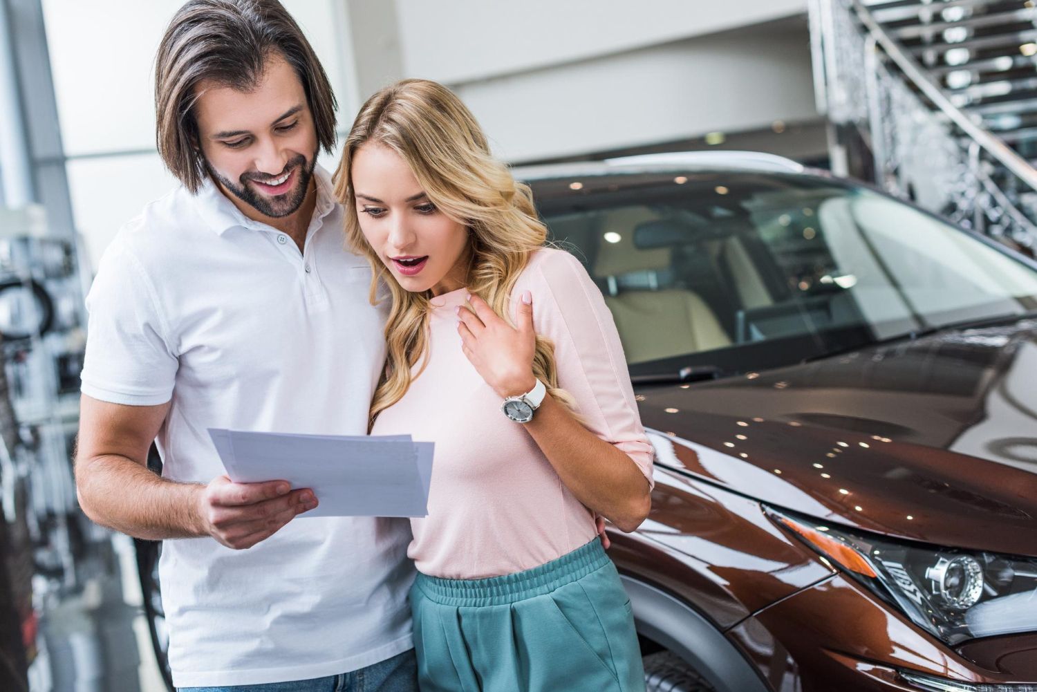 A man and a woman are looking at a piece of paper in front of a car.