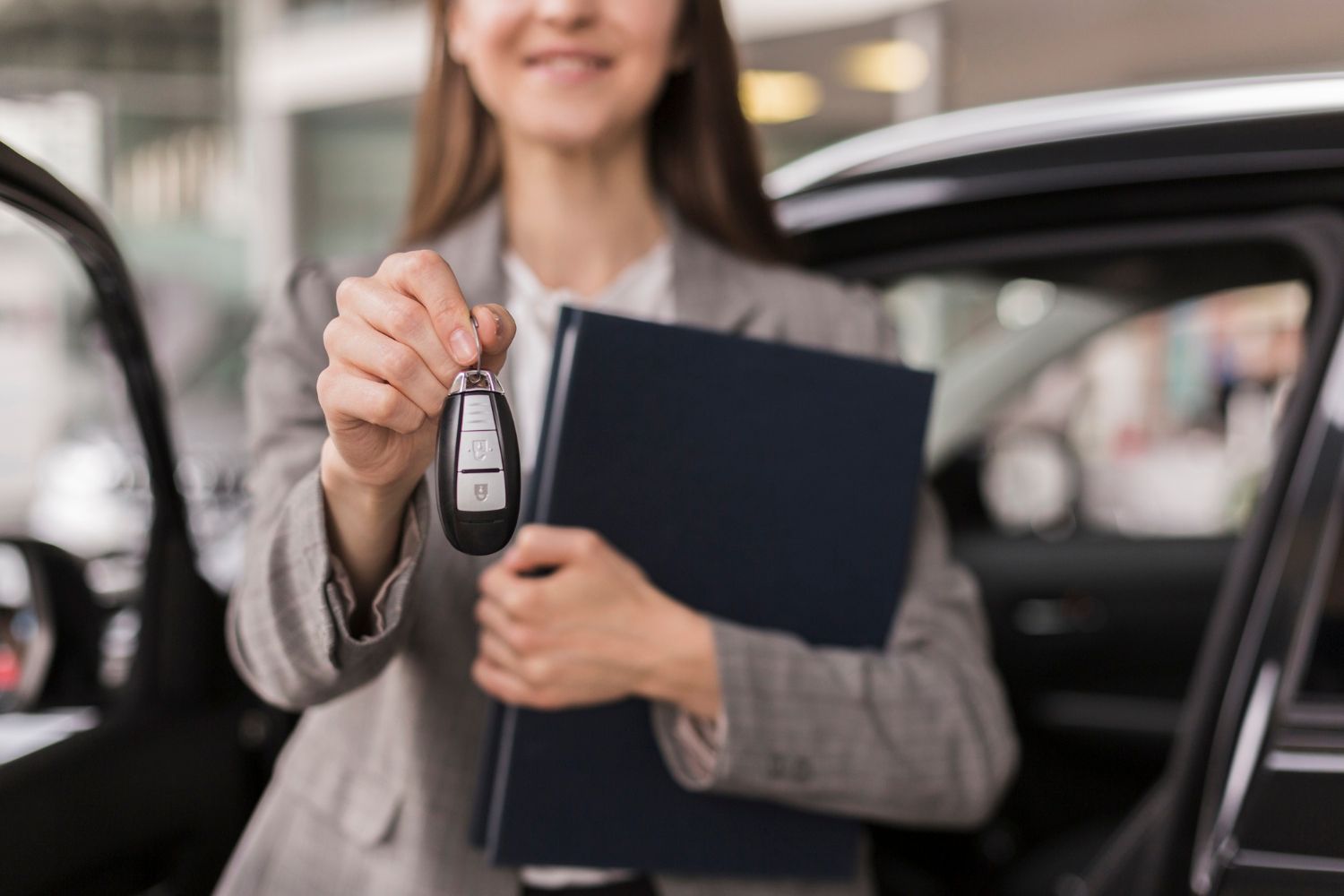 A woman is holding a folder and a car key in front of a car.