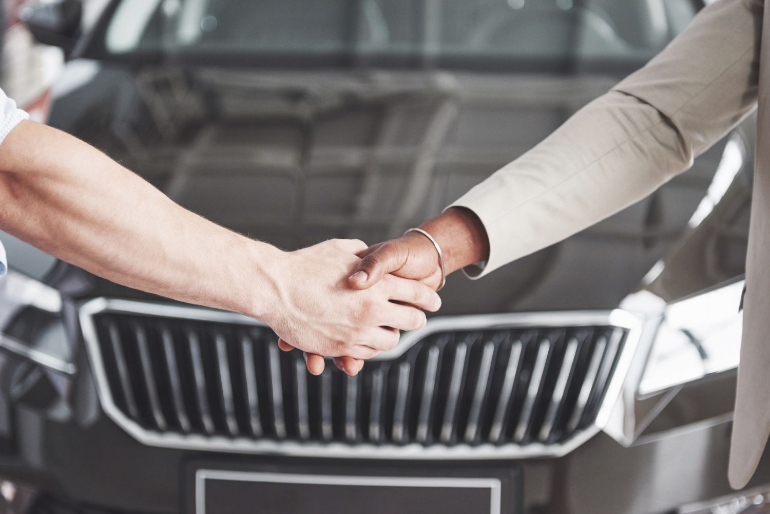 A man and a woman are shaking hands in front of a car.