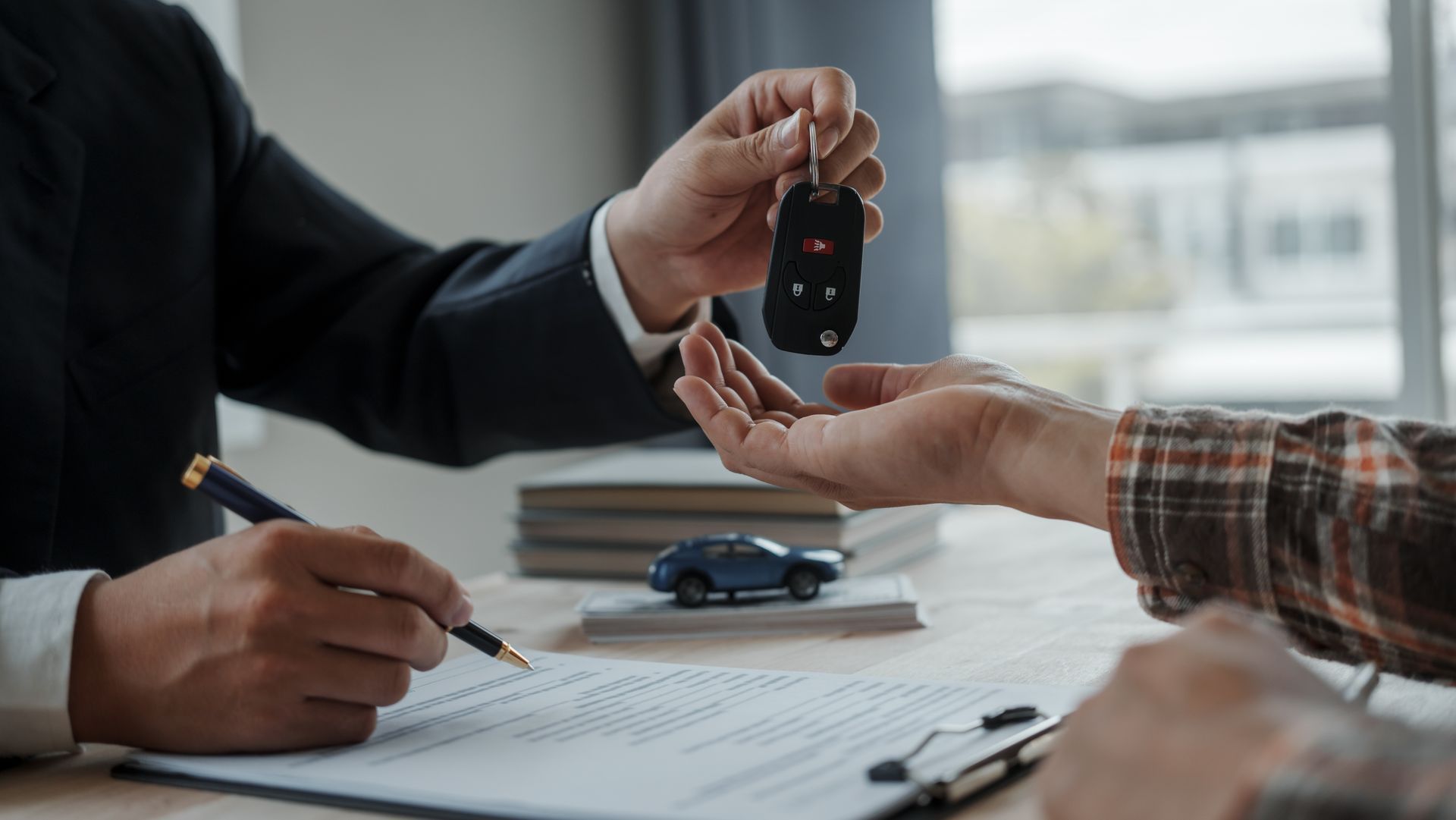 A man is giving a car key to another man while signing a contract.