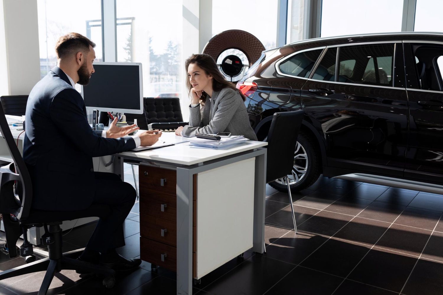 A man and a woman are sitting at a desk in a car showroom.