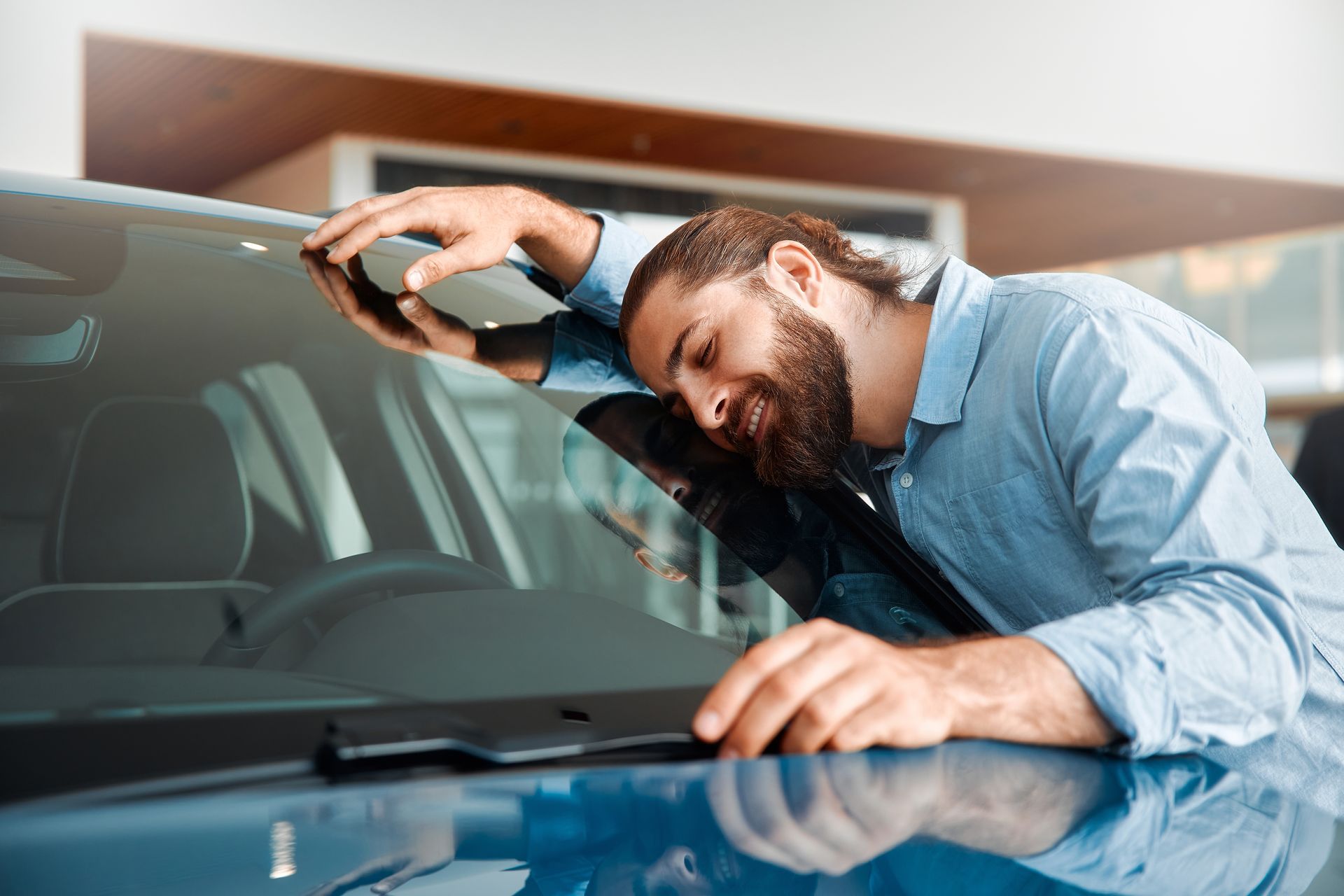 A man is looking at the windshield of a car in a showroom.