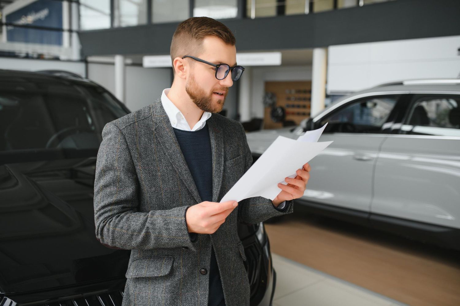 A man is looking at a piece of paper in a car showroom.