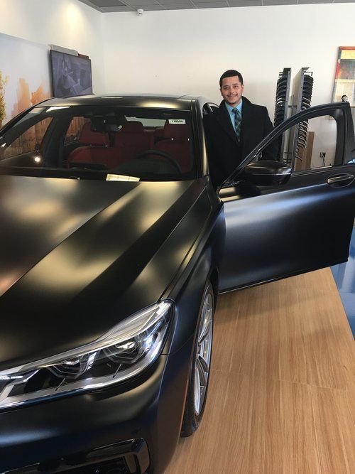 A man in a suit and tie is standing next to a black car.