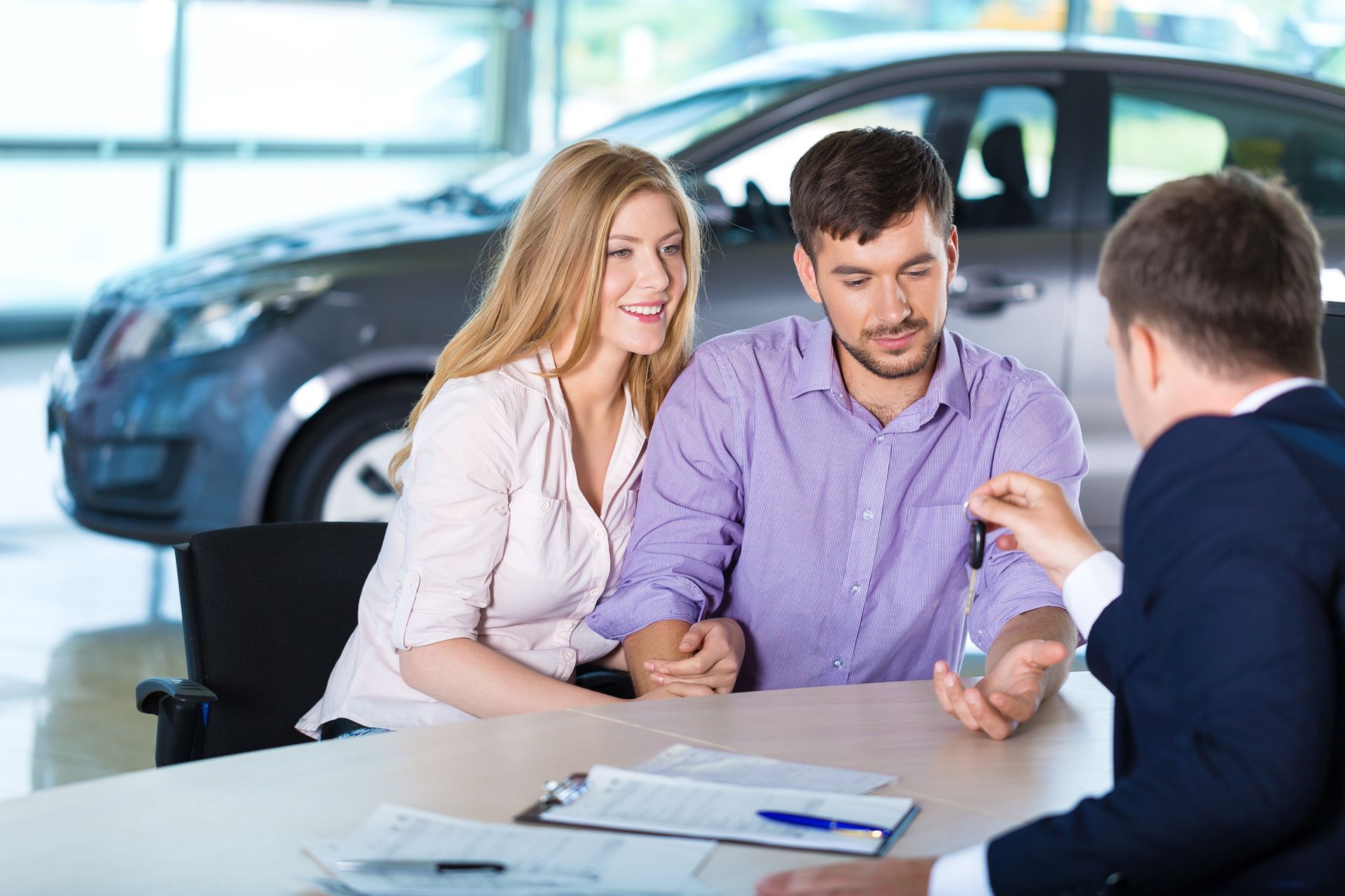 A man is giving a car key to a couple at a car dealership.