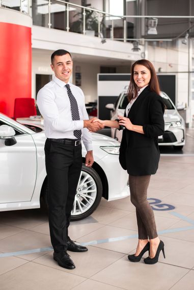A man and a woman are shaking hands in a car showroom.