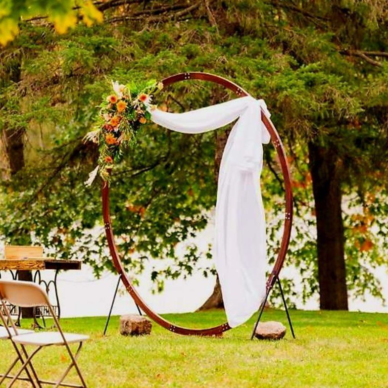Wedding arch with white fabric and floral arrangement in a grassy outdoor setting.