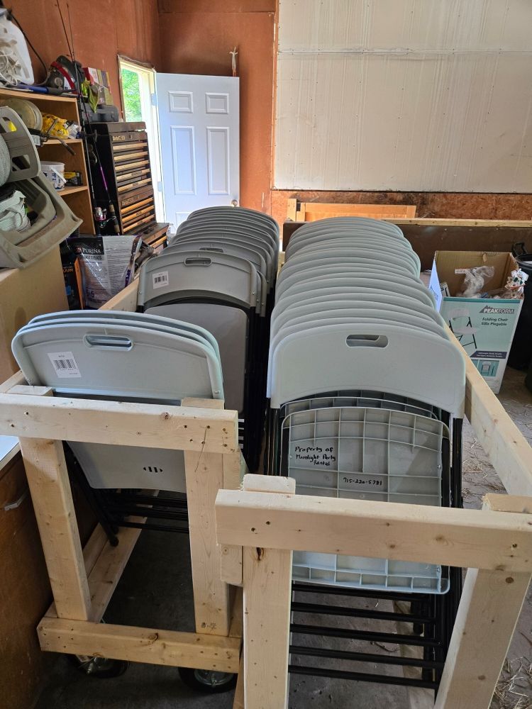 Wooden cart holding stacked gray and white plastic folding chairs in a garage.