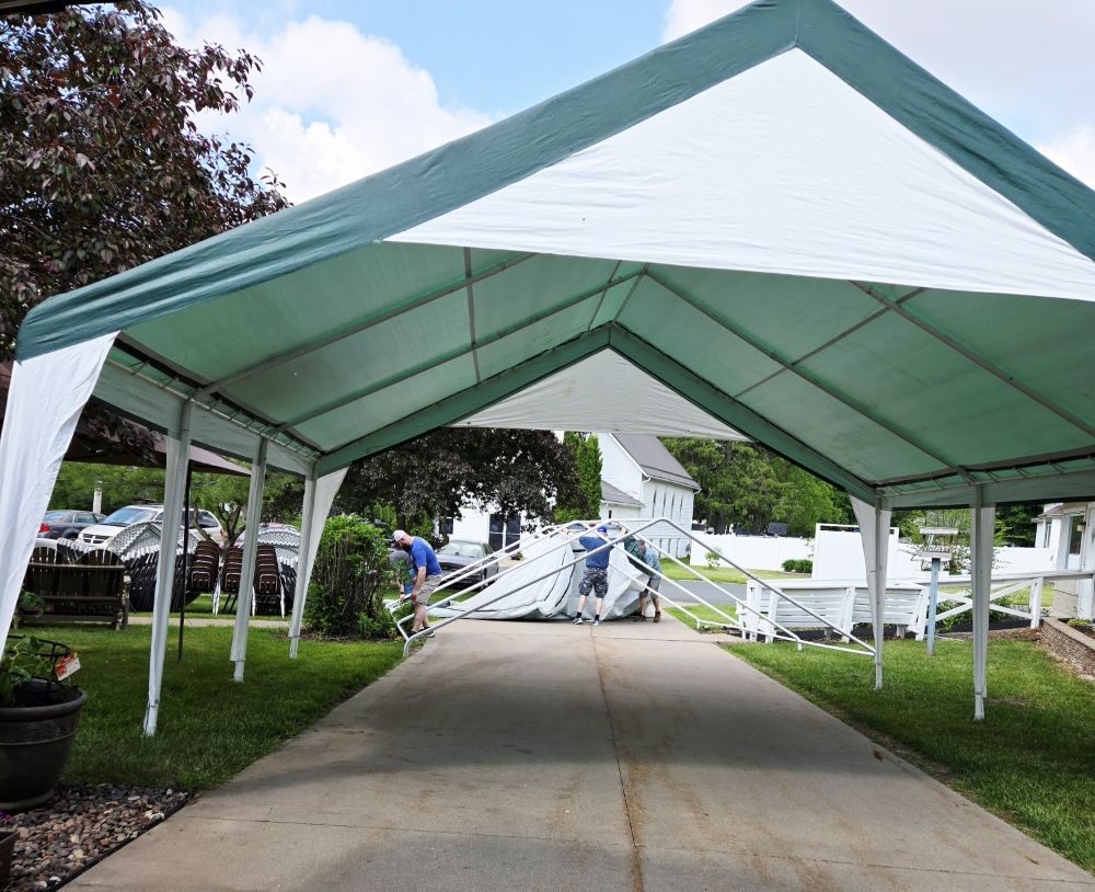 Green and white canopy being assembled on a driveway. Two people work on the structure.