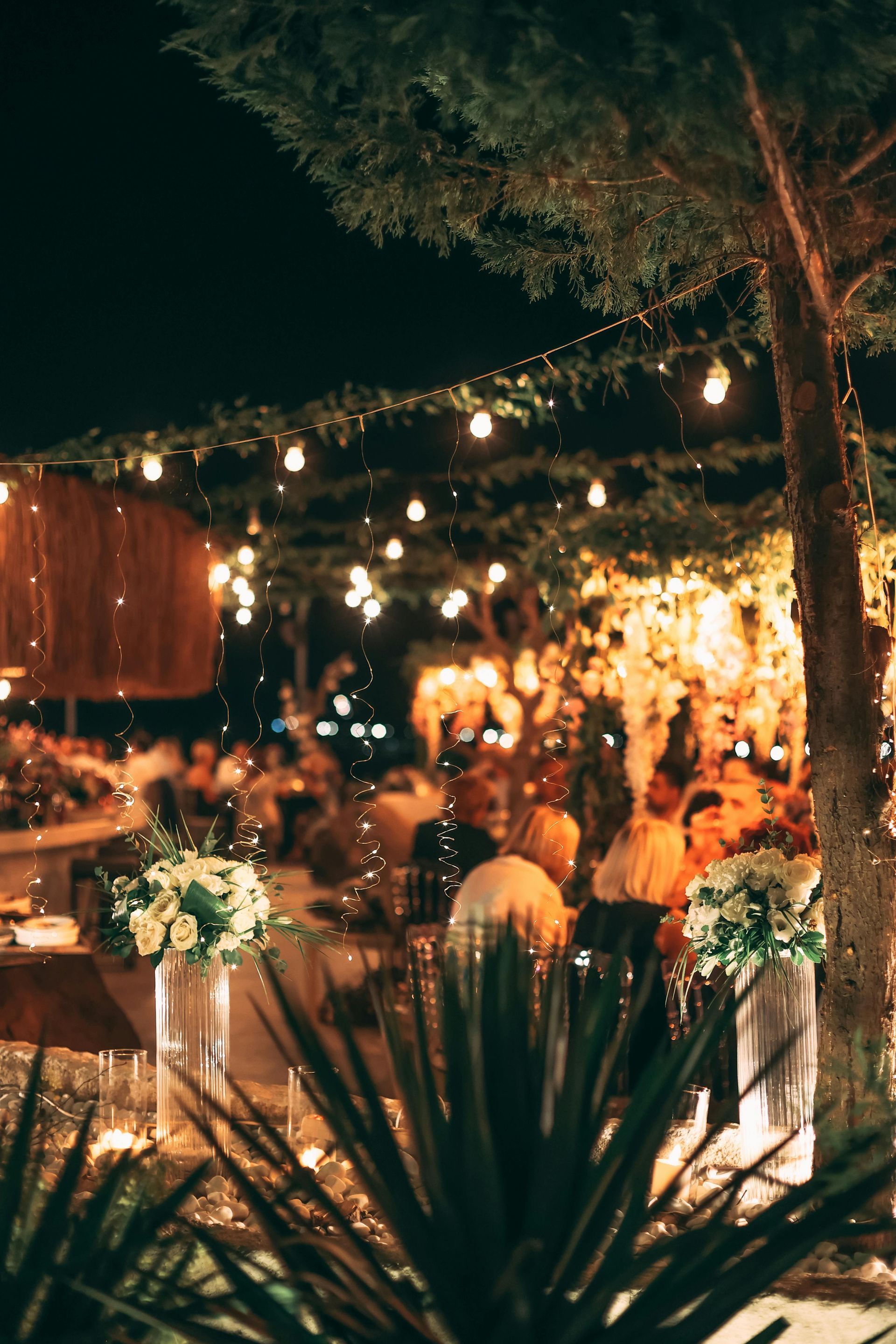 Nighttime outdoor event with string lights and floral arrangements.
