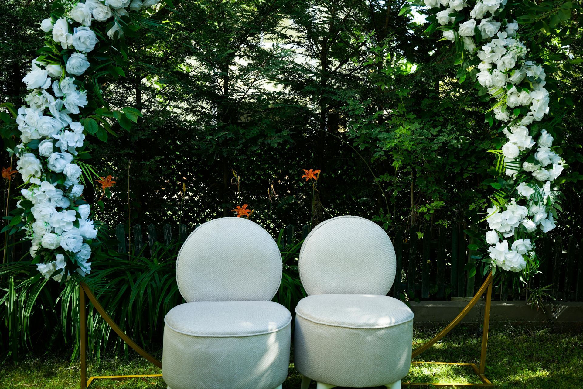 Two white chairs under a floral arch in a garden setting.