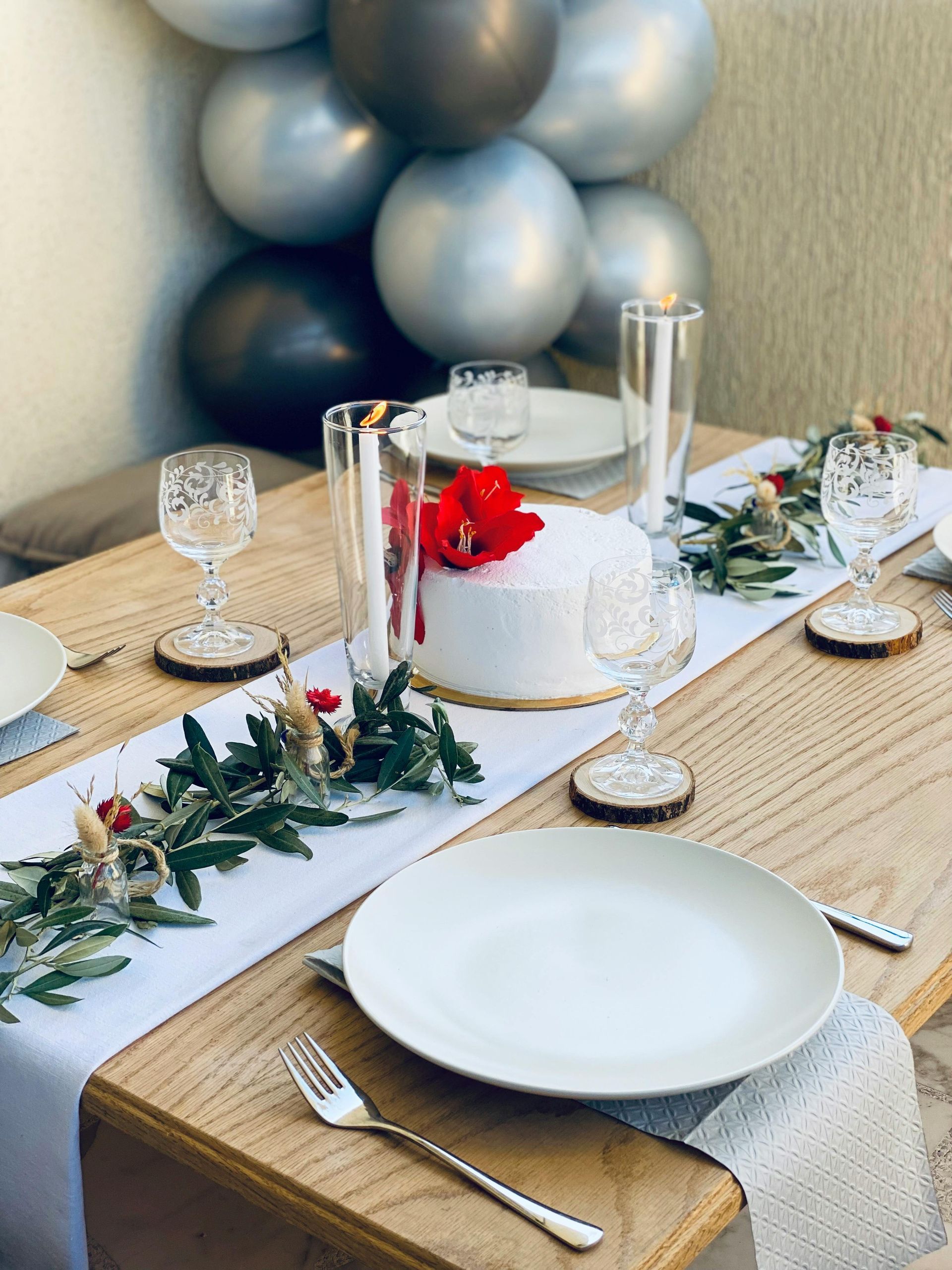 Festive outdoor table setting with white cake, floral garland, plates, silverware, and balloons.