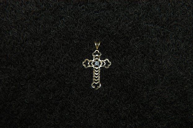 A small silver cross is sitting on a black surface.