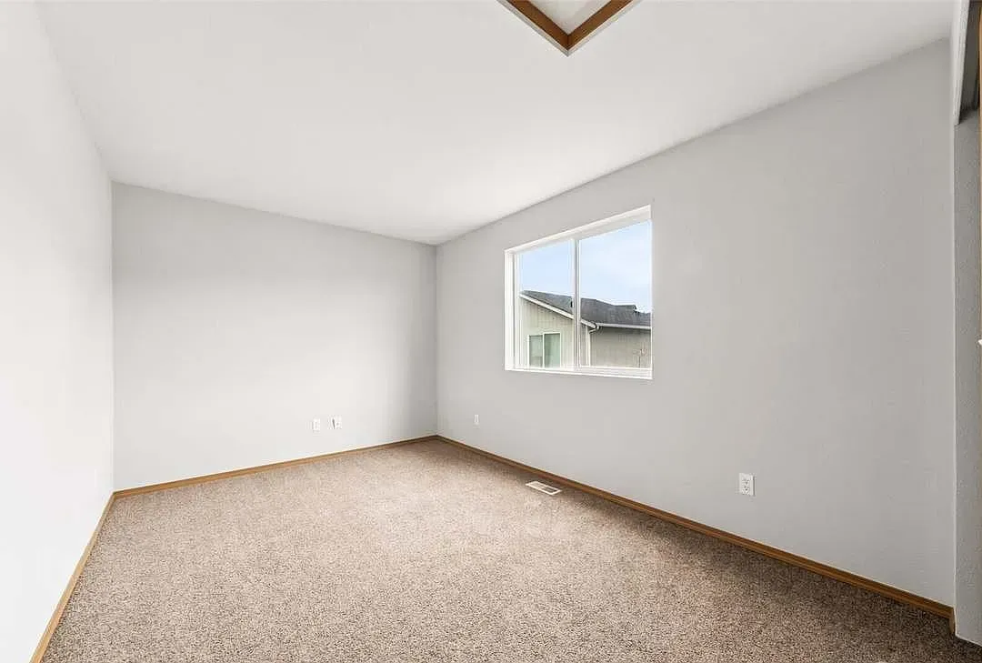 Empty room with beige carpet, gray walls, a window, and a light fixture.