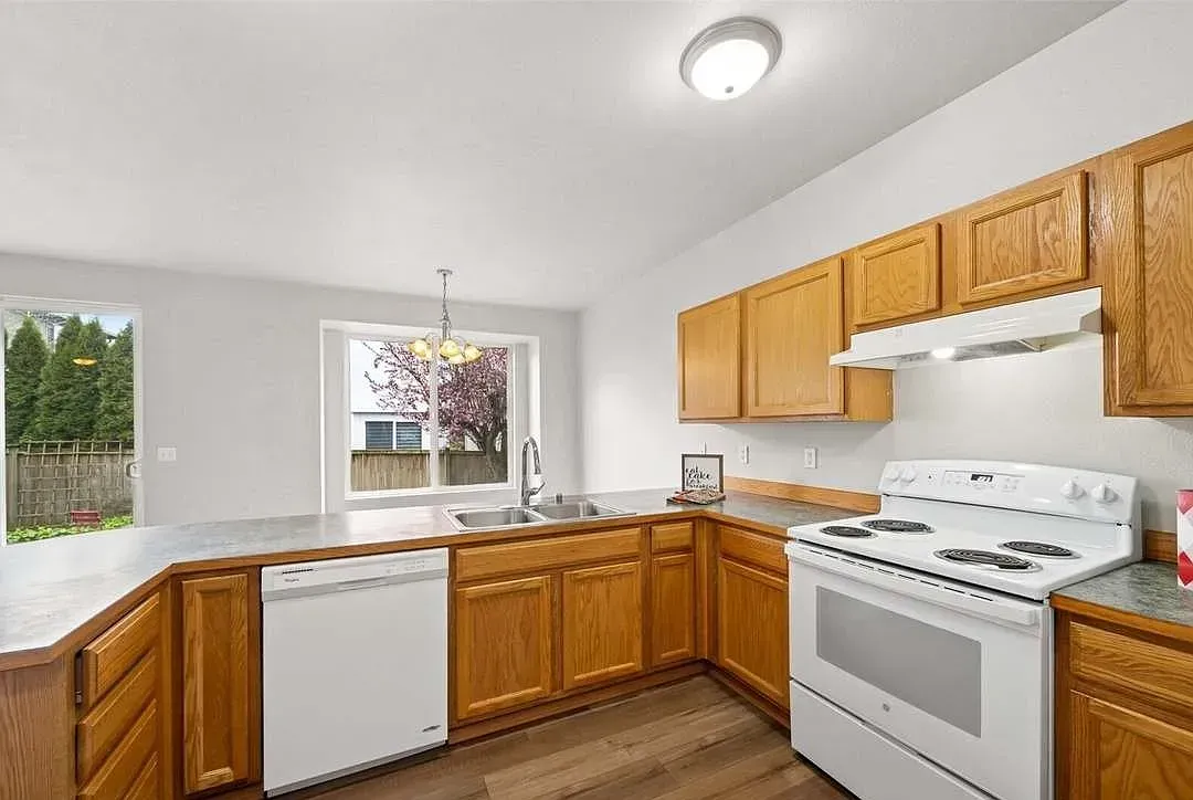 Kitchen with wooden cabinets, white appliances, and a window overlooking a yard.