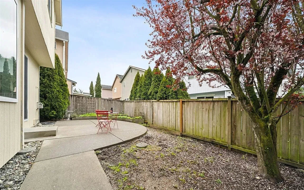 Backyard patio with red tree, wooden fence, and concrete path.