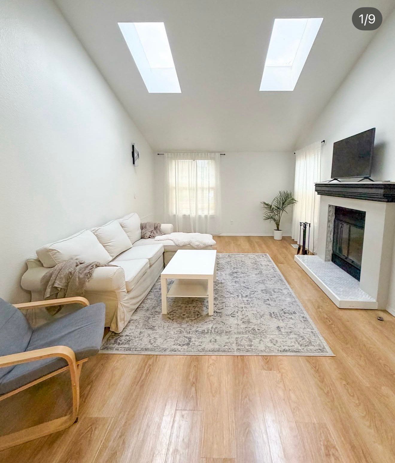 Bright living room with white walls, skylights, and a white sofa. Fireplace and wooden floors.