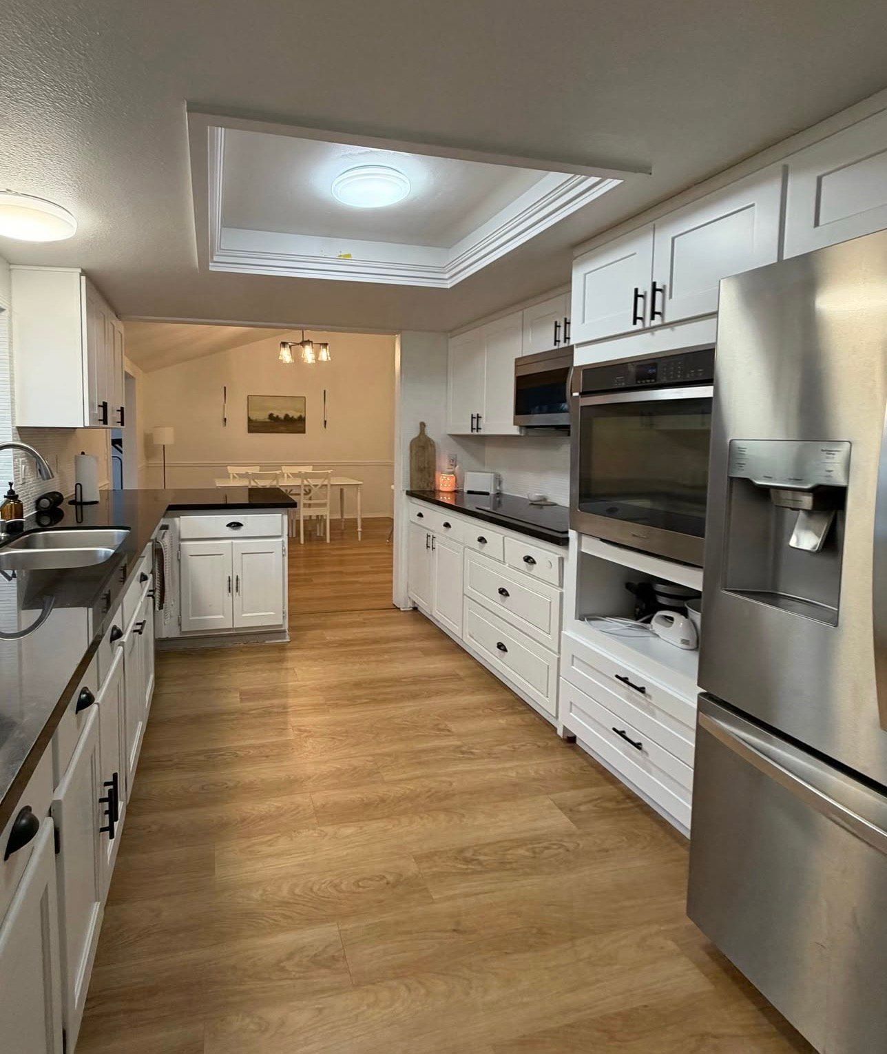 Modern white kitchen with stainless steel appliances, dark countertops, and light wood floors.