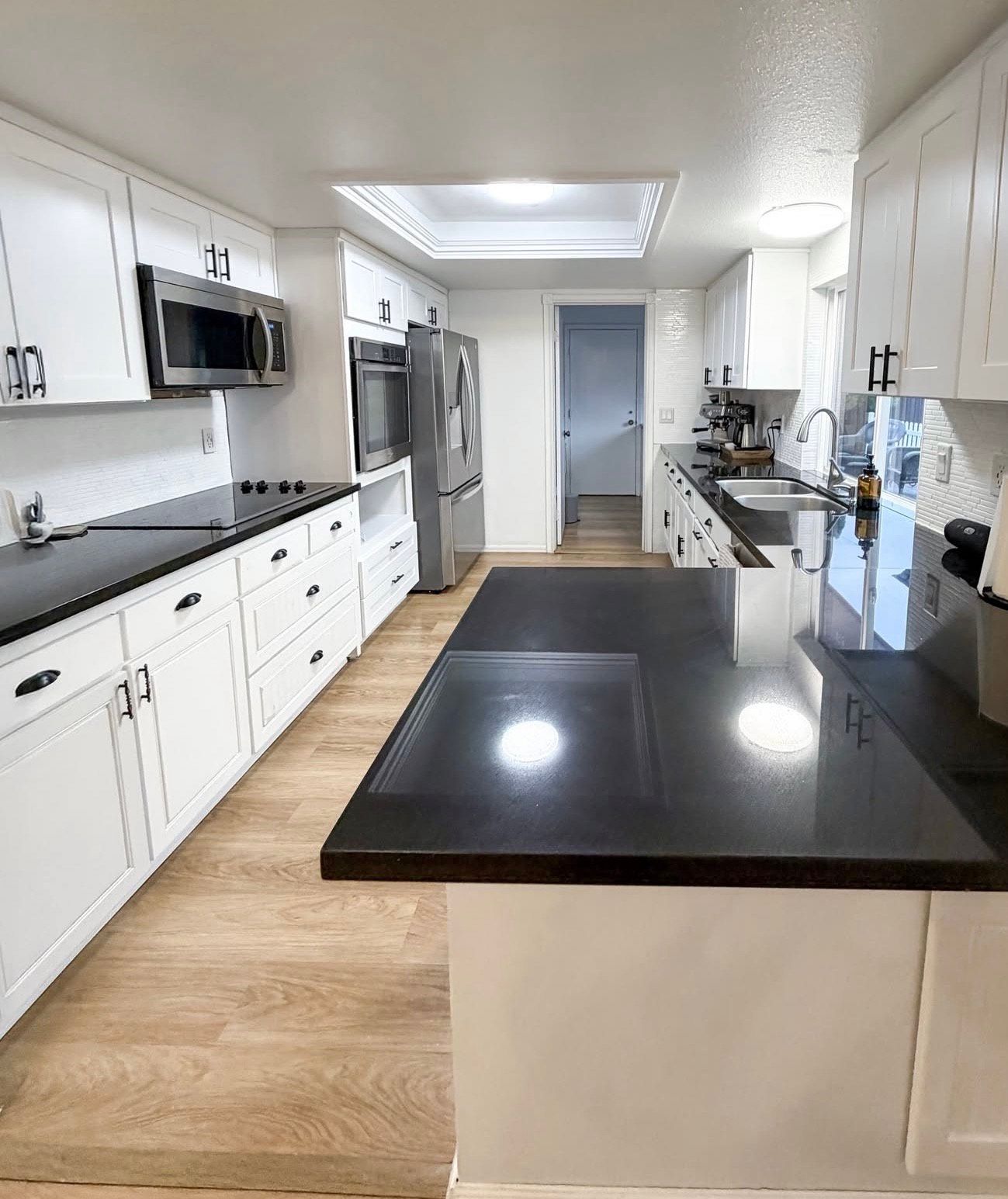White kitchen with black countertops, stainless steel appliances, and wood-look flooring.