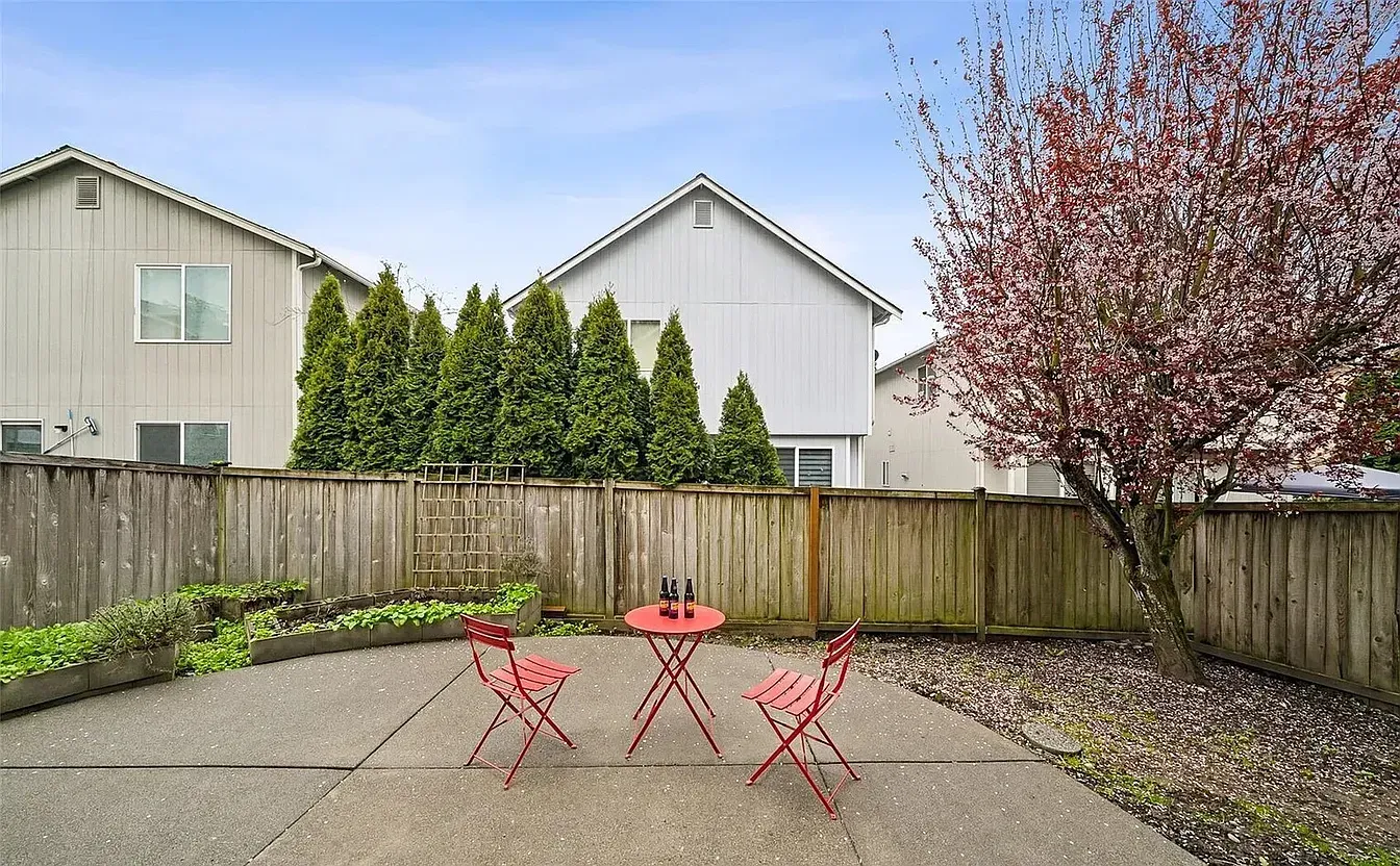 A small backyard with a red table and chairs on a concrete patio, fence, and a flowering tree.
