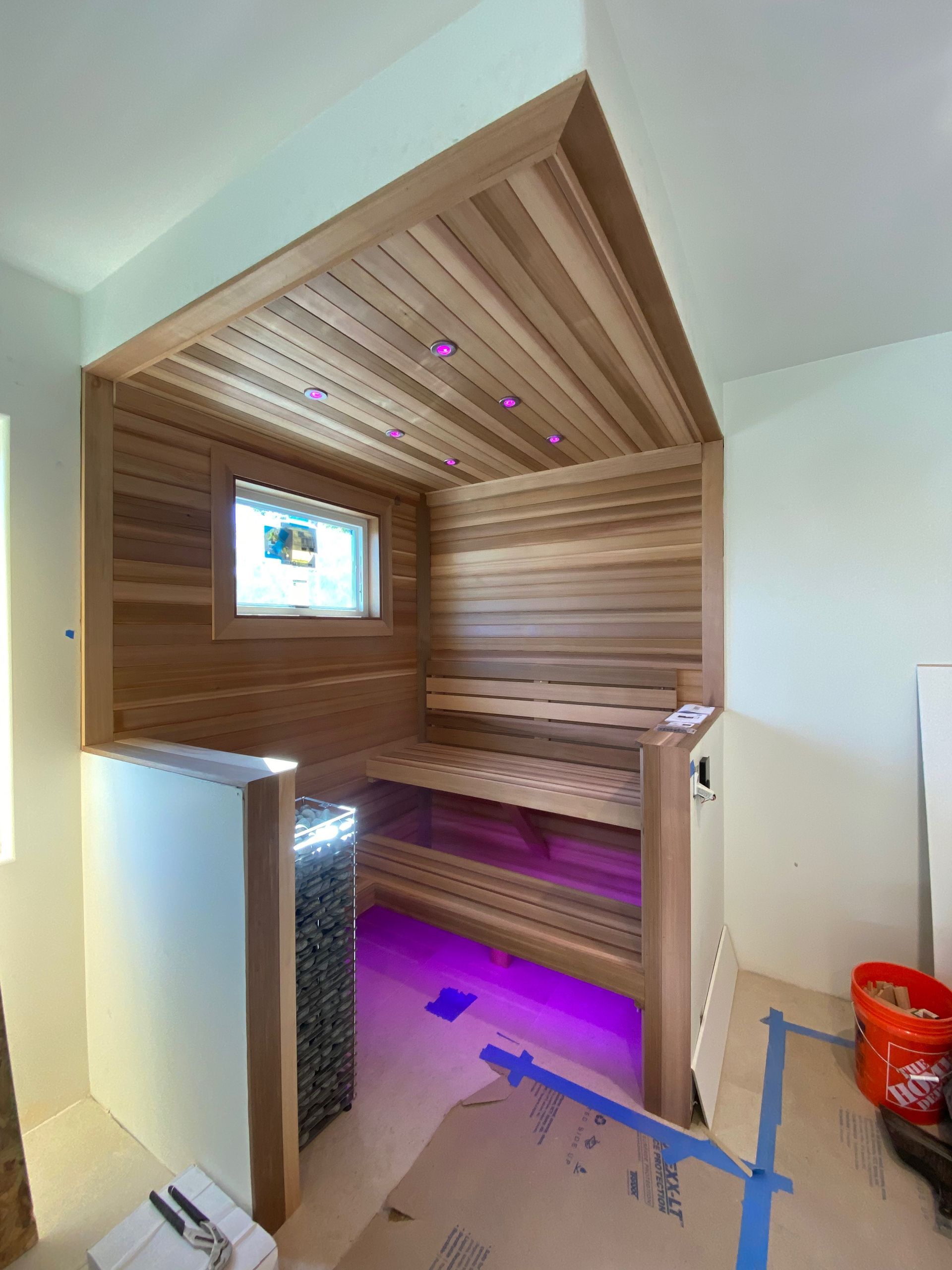 A cedar wood sauna under construction with interior lighting and a small screen.