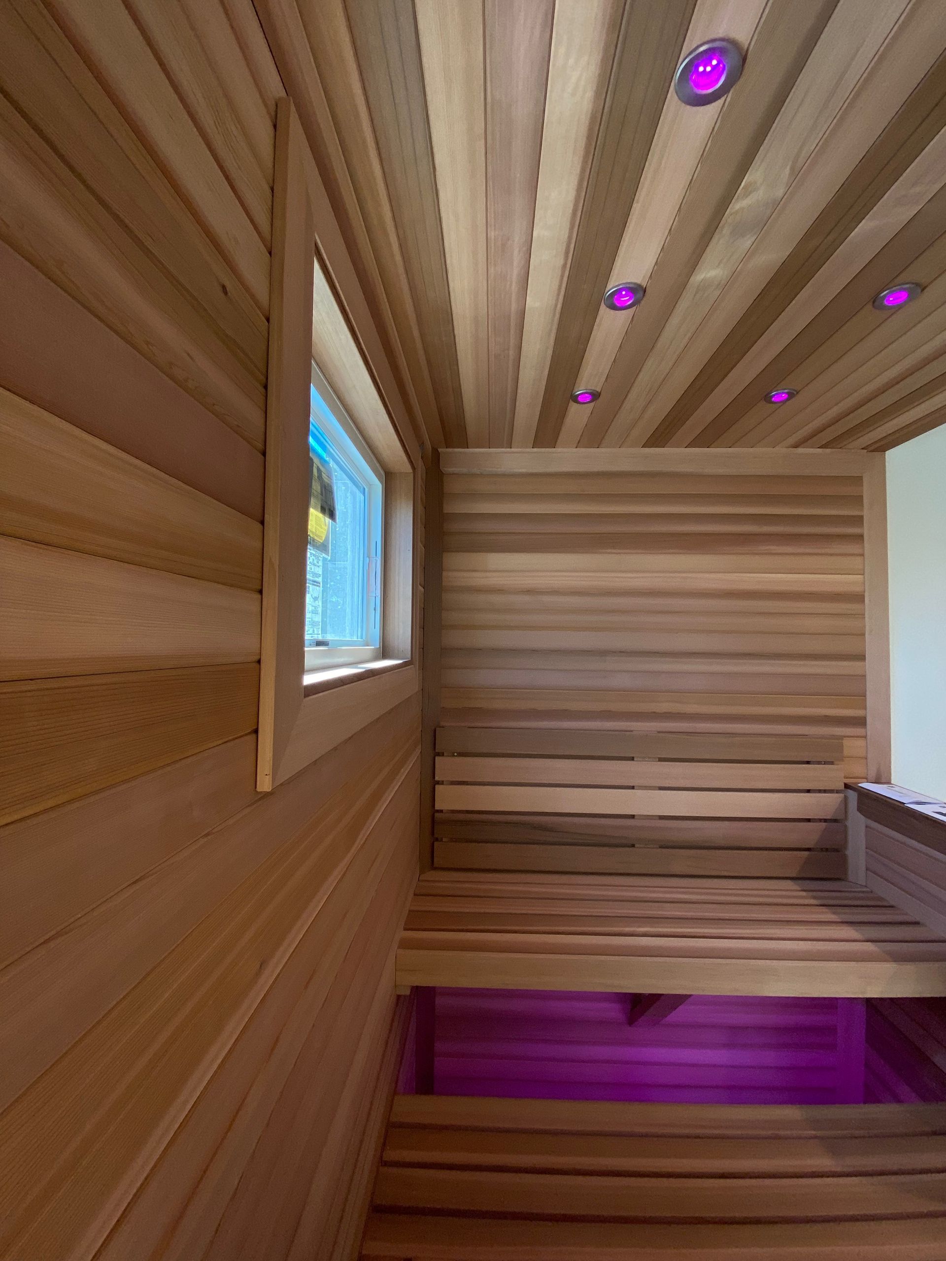 Wooden sauna interior with window and purple lighting.