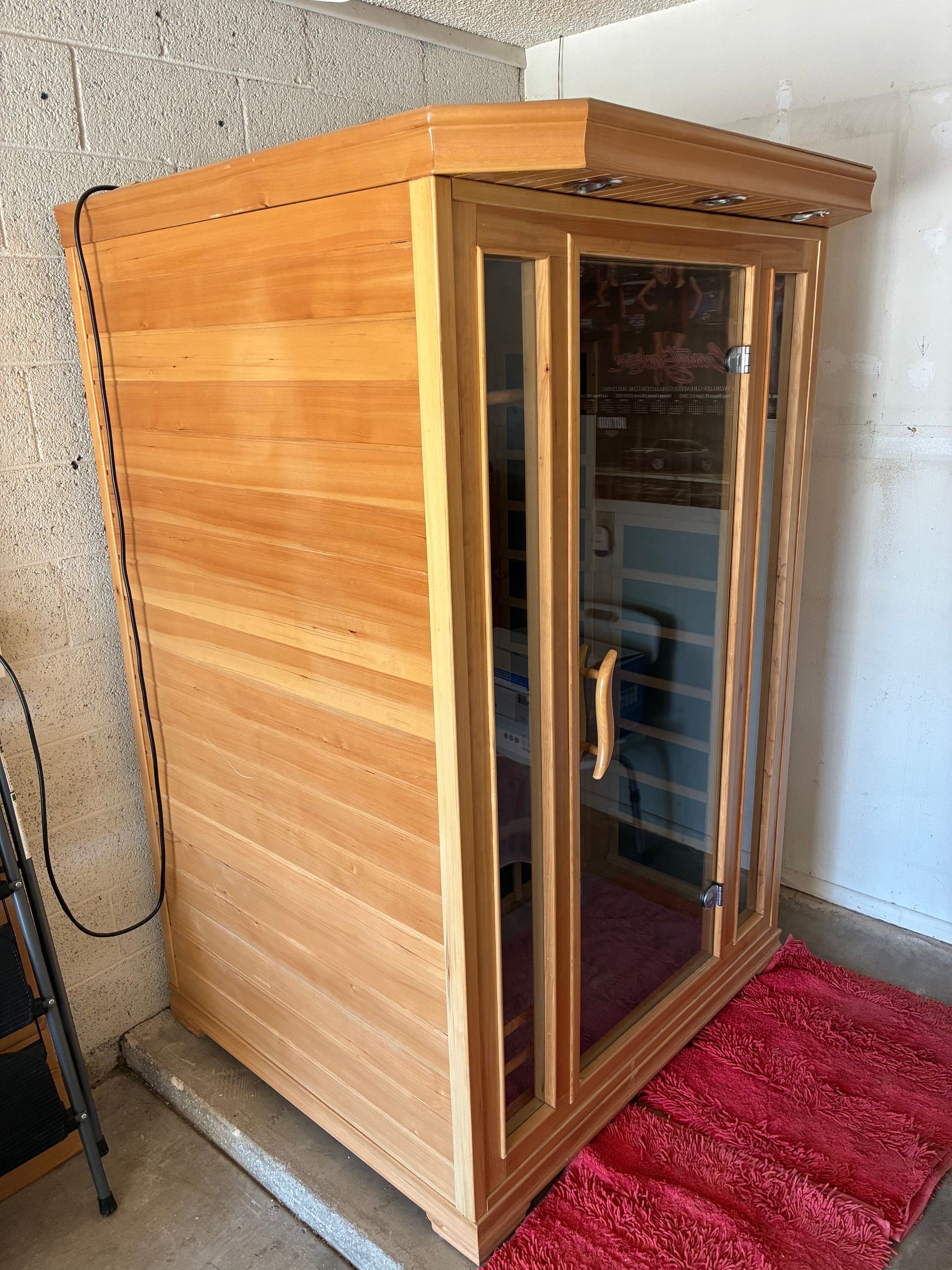 Wooden sauna with glass door, red mat, in a garage.