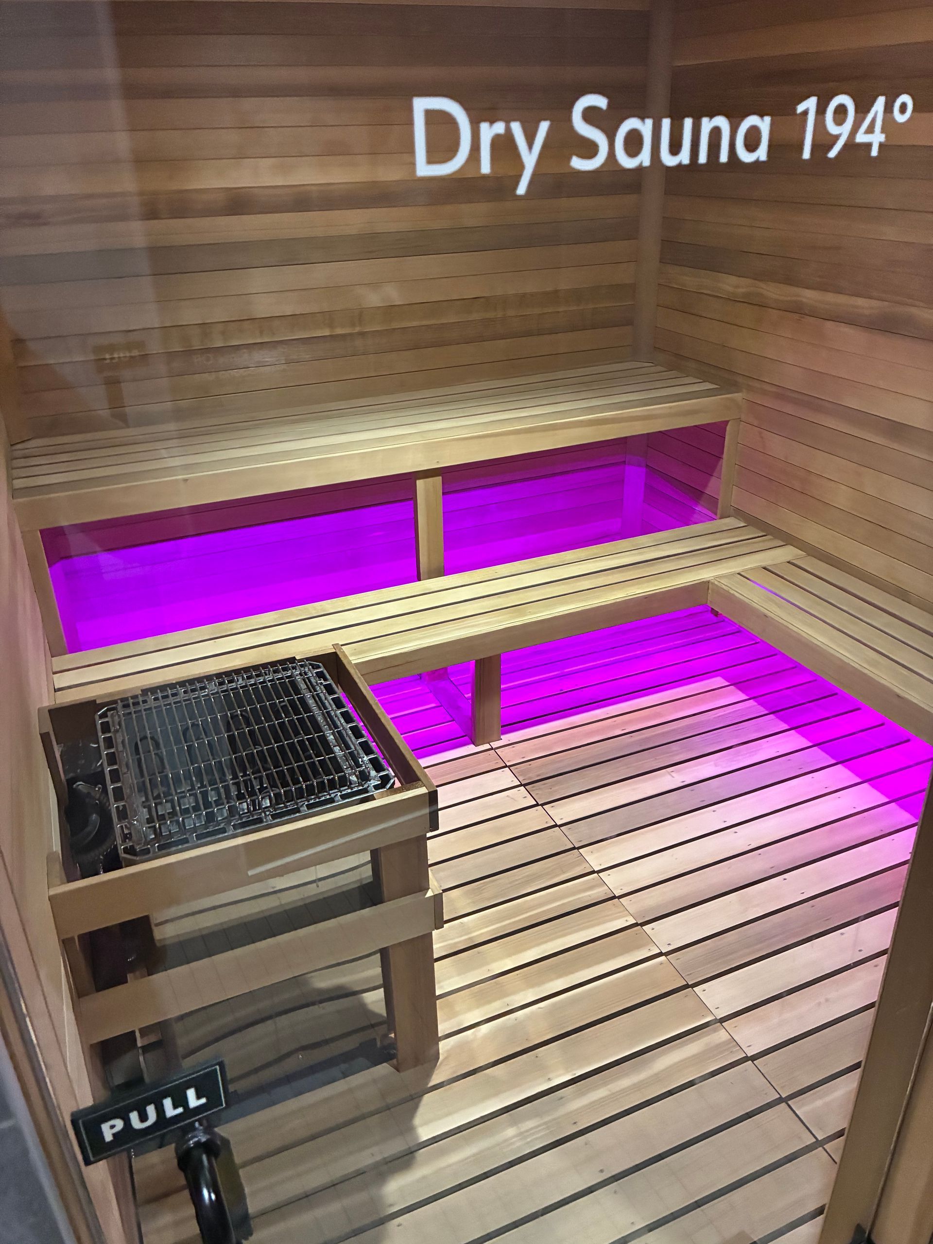 Dry sauna with wooden benches and floor, lit with purple lights. Sauna temperature reads 194 degrees.