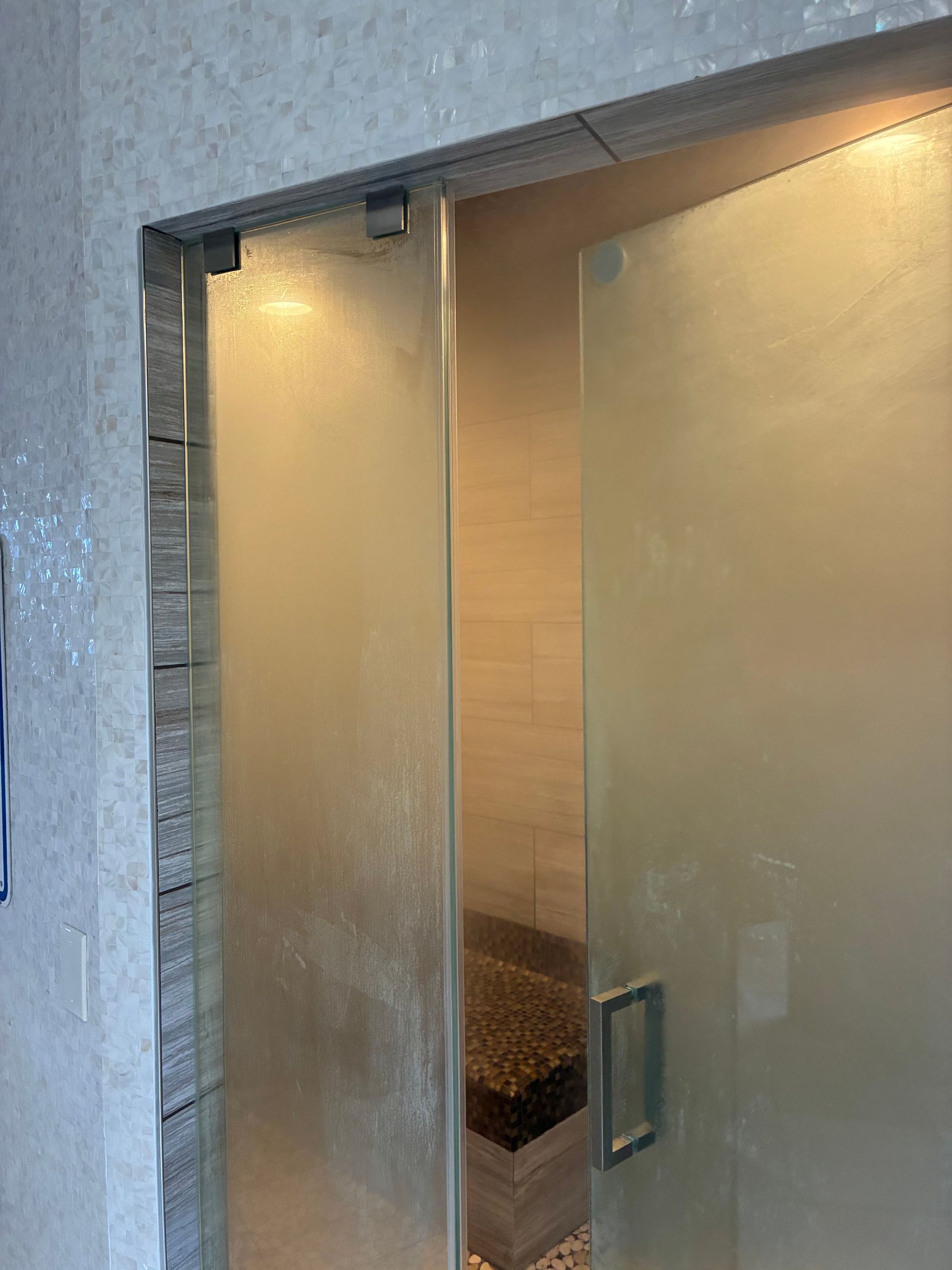 Shower with frosted glass door and a small bench inside. Gray and beige tones.