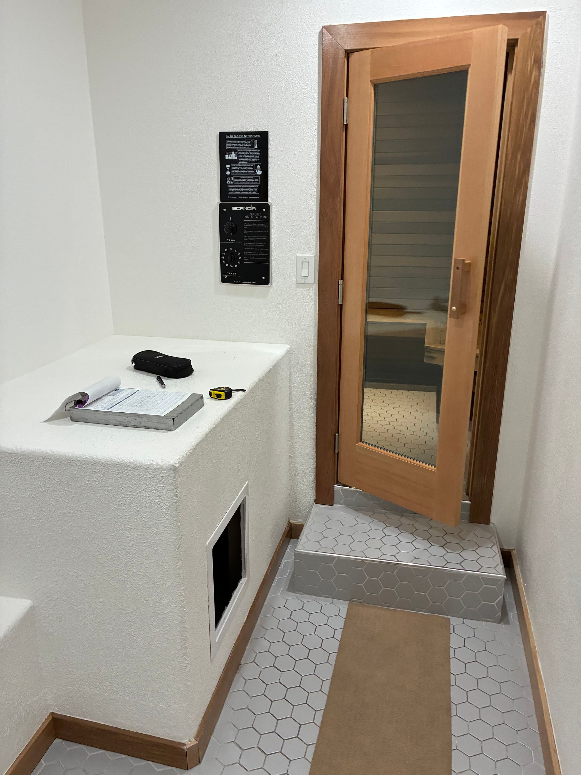 A sauna entrance with a small step, tiled floor, and a white, textured structure with instructions.
