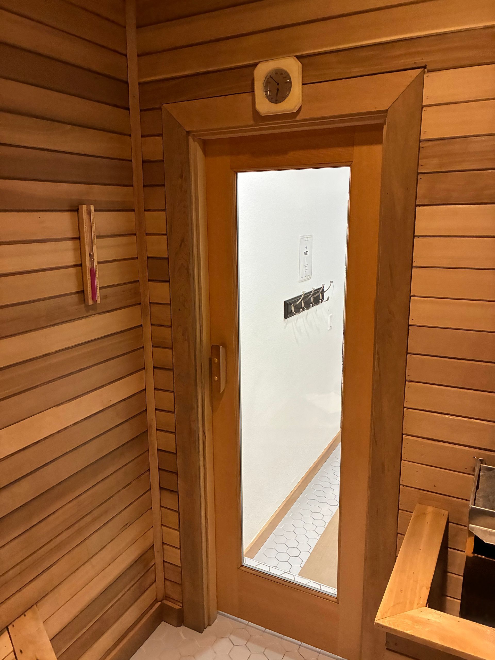 Interior view of a sauna with wooden walls, door, and bench. A thermometer hangs on the wall.