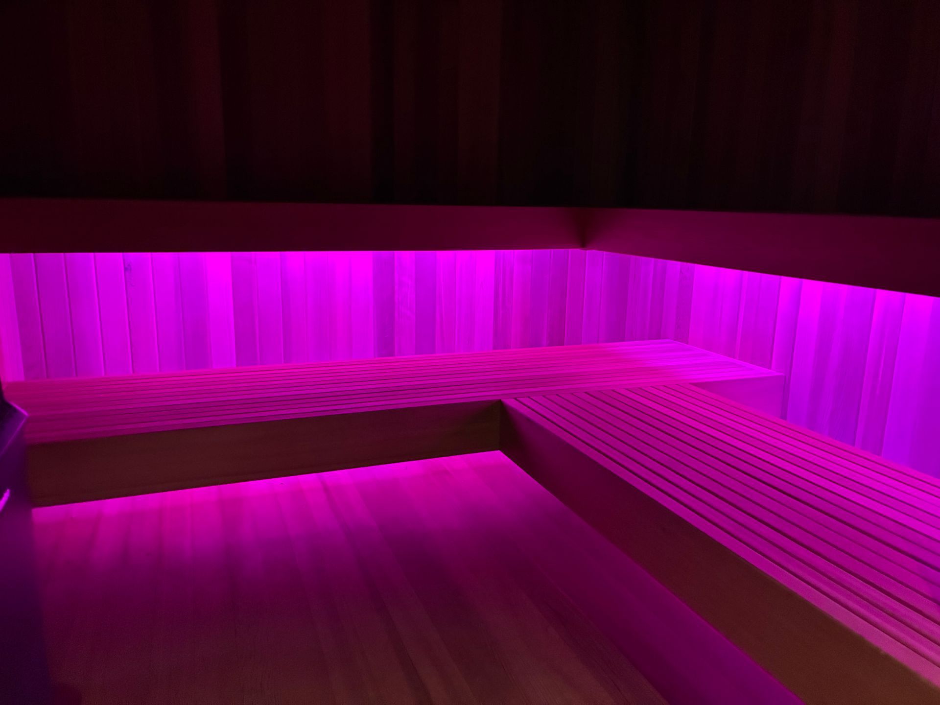 Interior of a sauna with pink LED lighting under benches and along the walls.