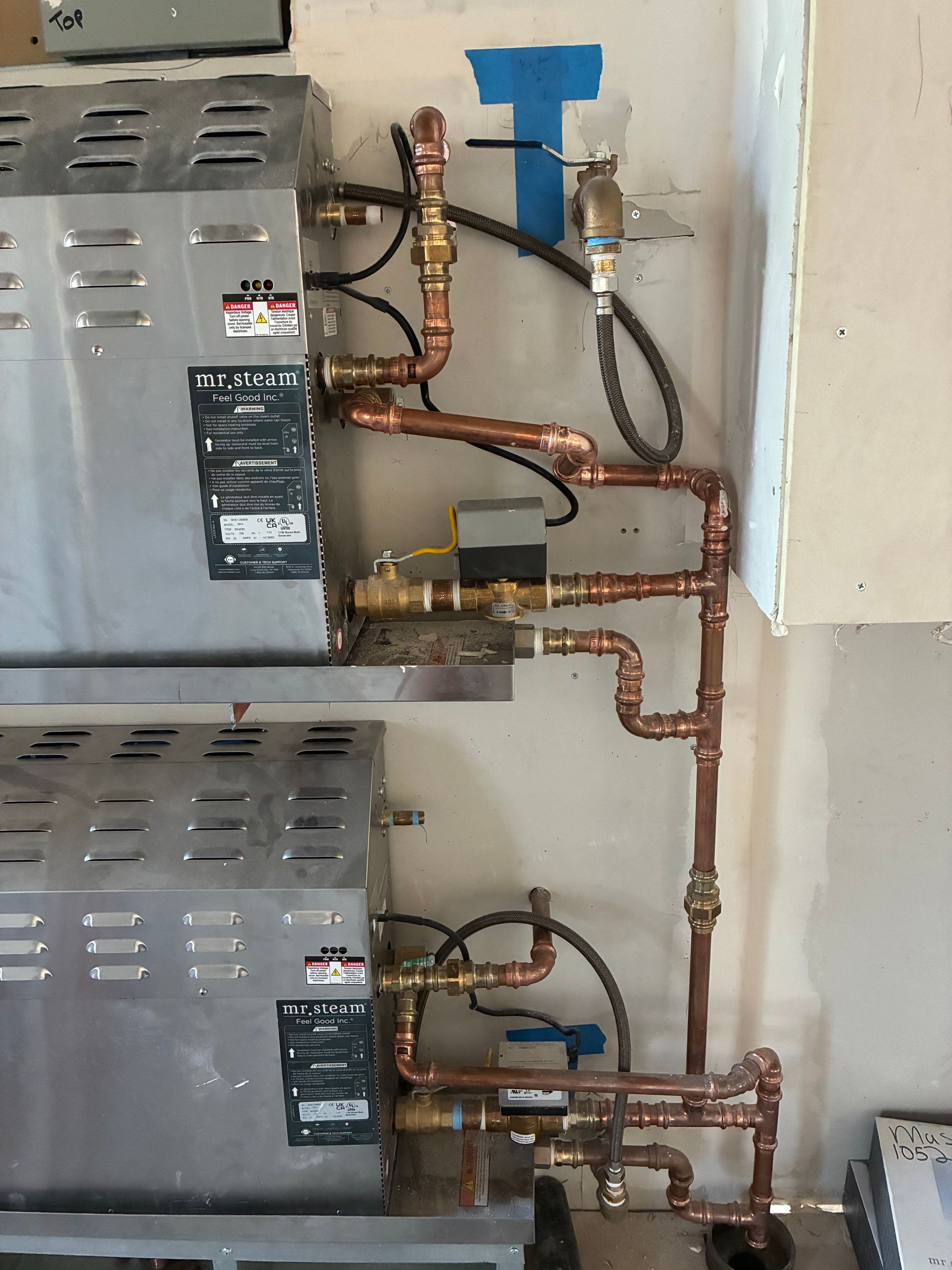Two metal water heaters with copper pipes against a wall.