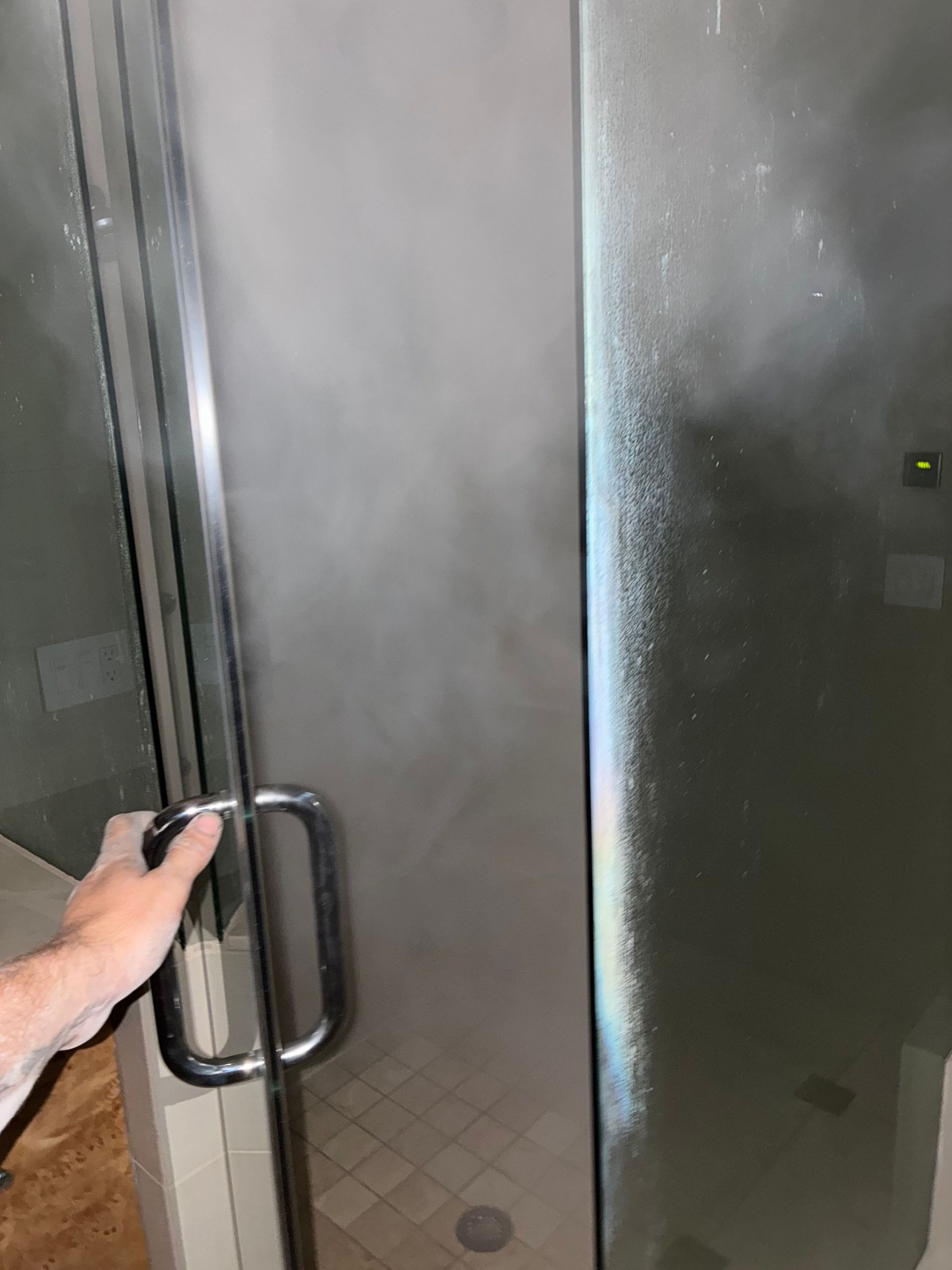 Hand opening a glass shower door with a metal handle, frosted glass, and stone wall in the bathroom.