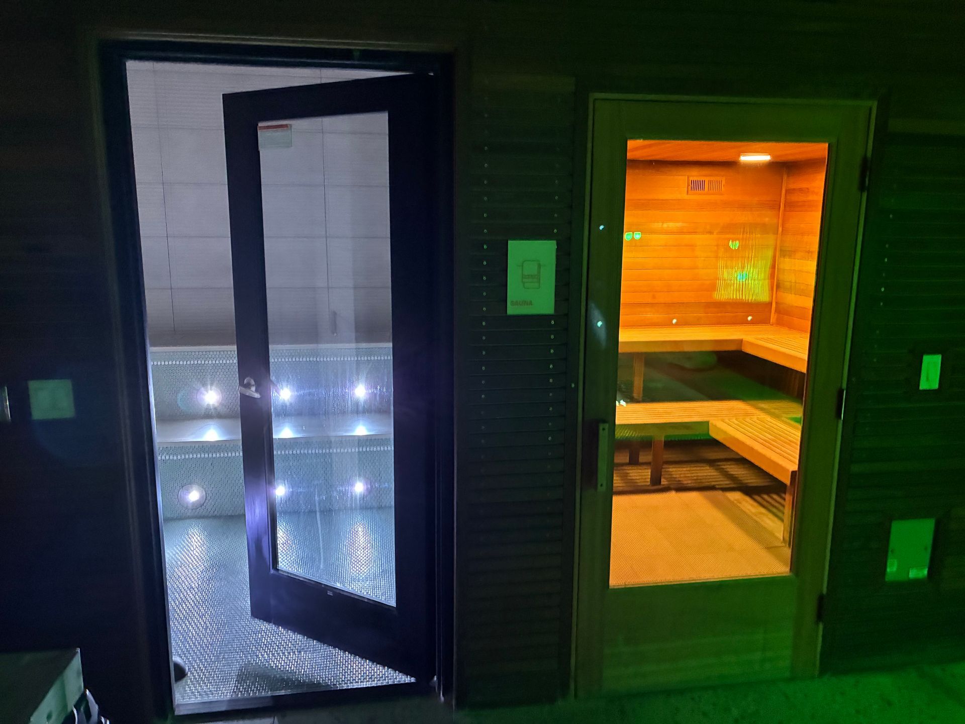 Open doors to a pool with lights and a sauna with wooden benches, side by side.