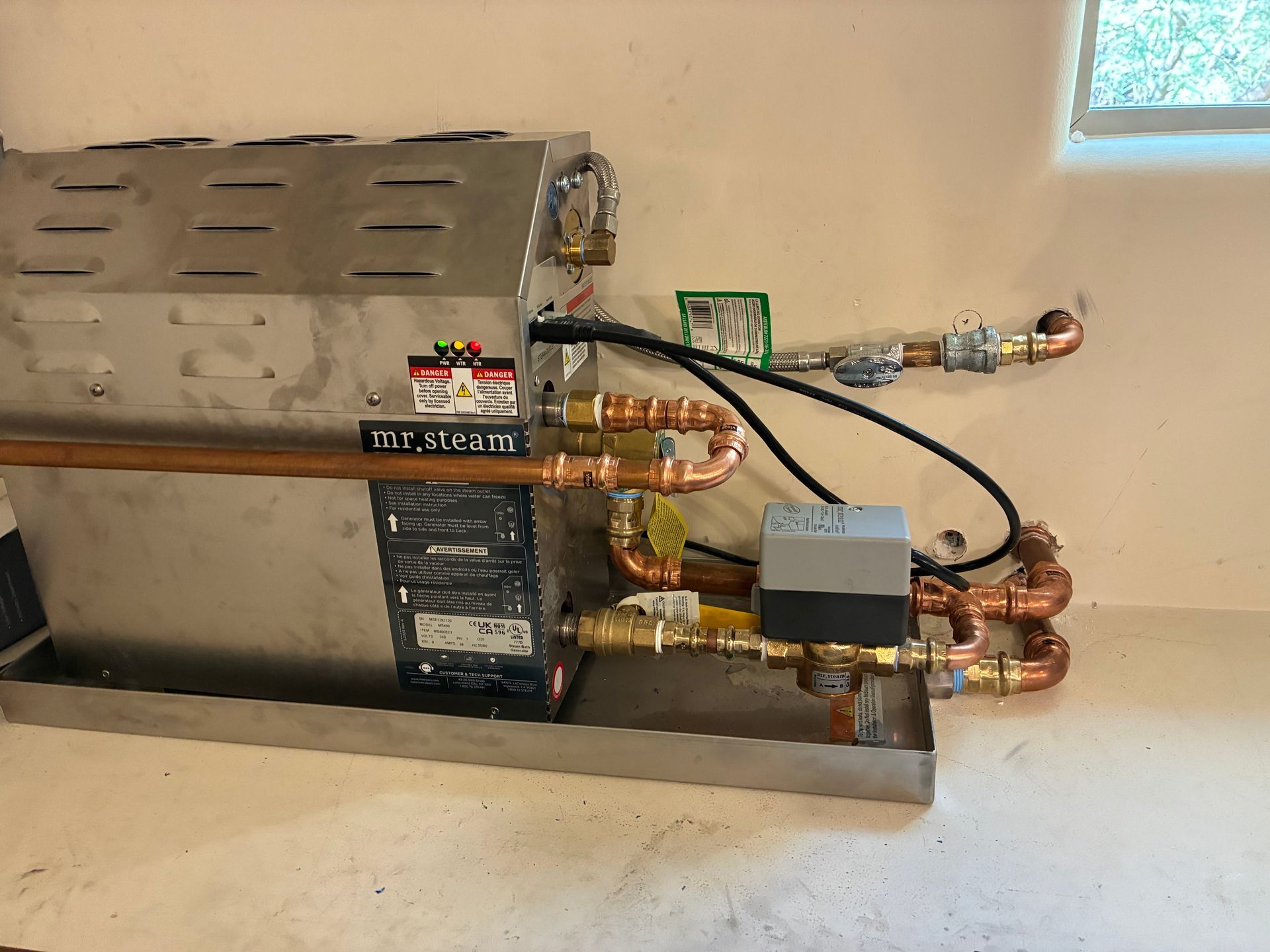 Mr. Steam steam generator with copper pipes and electrical components installed on a wall.