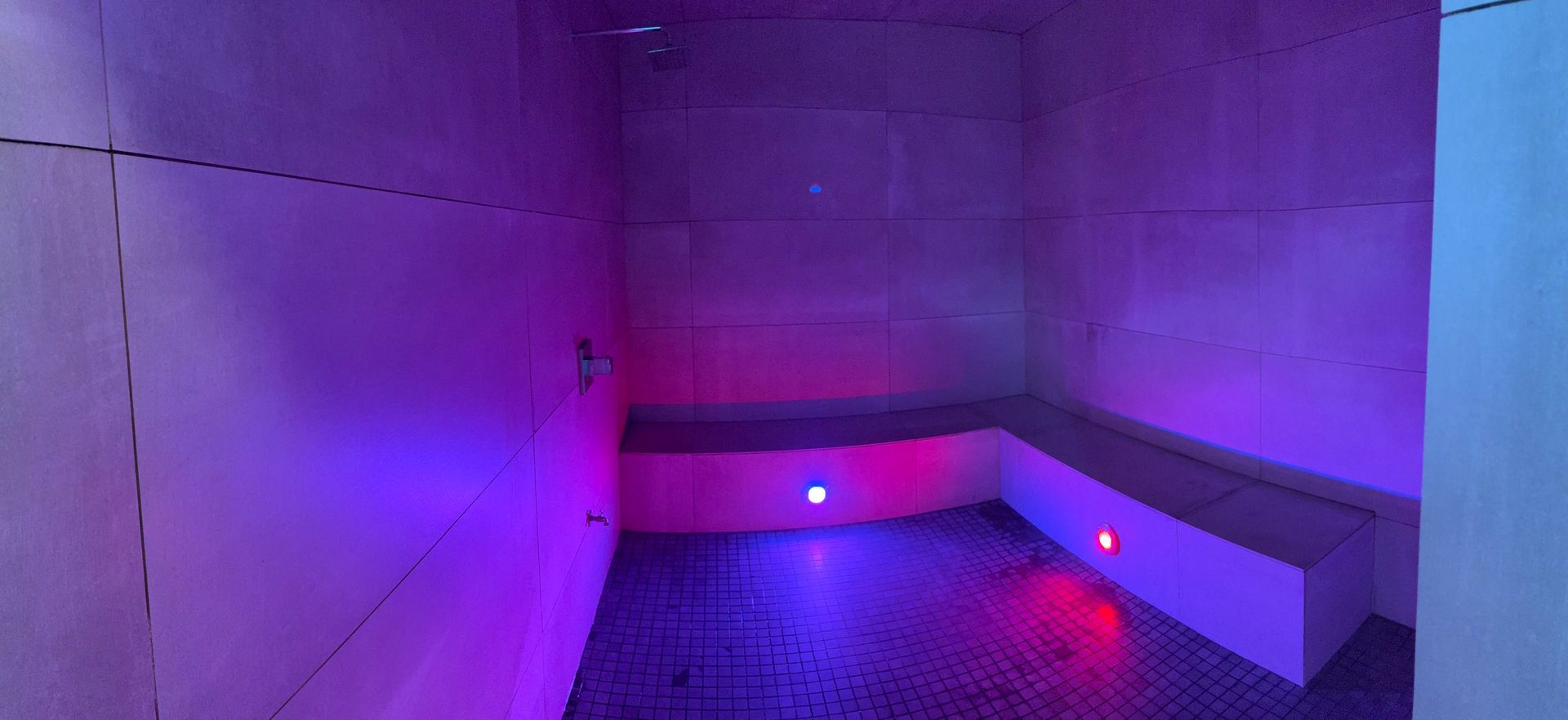 Purple-lit steam room with a bench. Red and blue lights illuminate the floor.