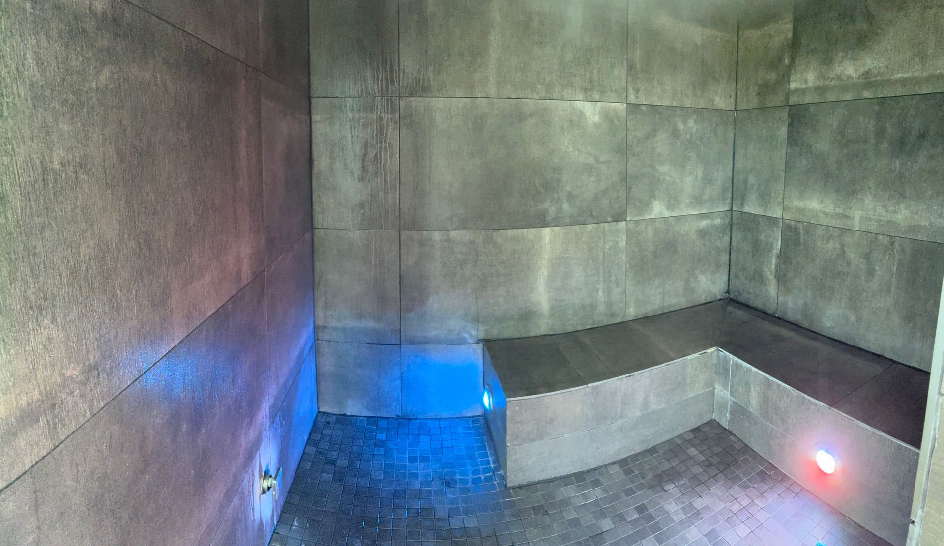 Stone-walled sauna with curved built-in benches, lit with blue and red lights.