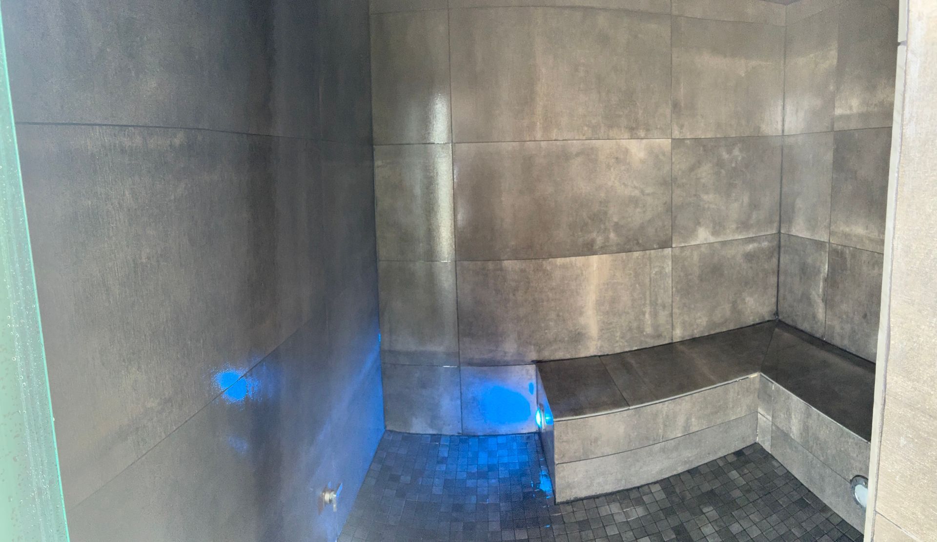 Gray tiled shower with built-in bench. Blue markings are on the floor and wall.