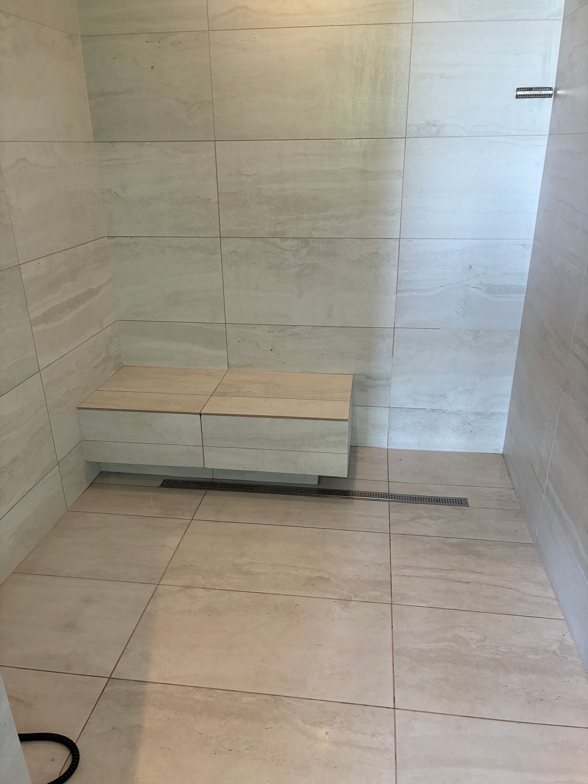 Shower with beige tile walls and floor; a built-in bench is on the left wall.