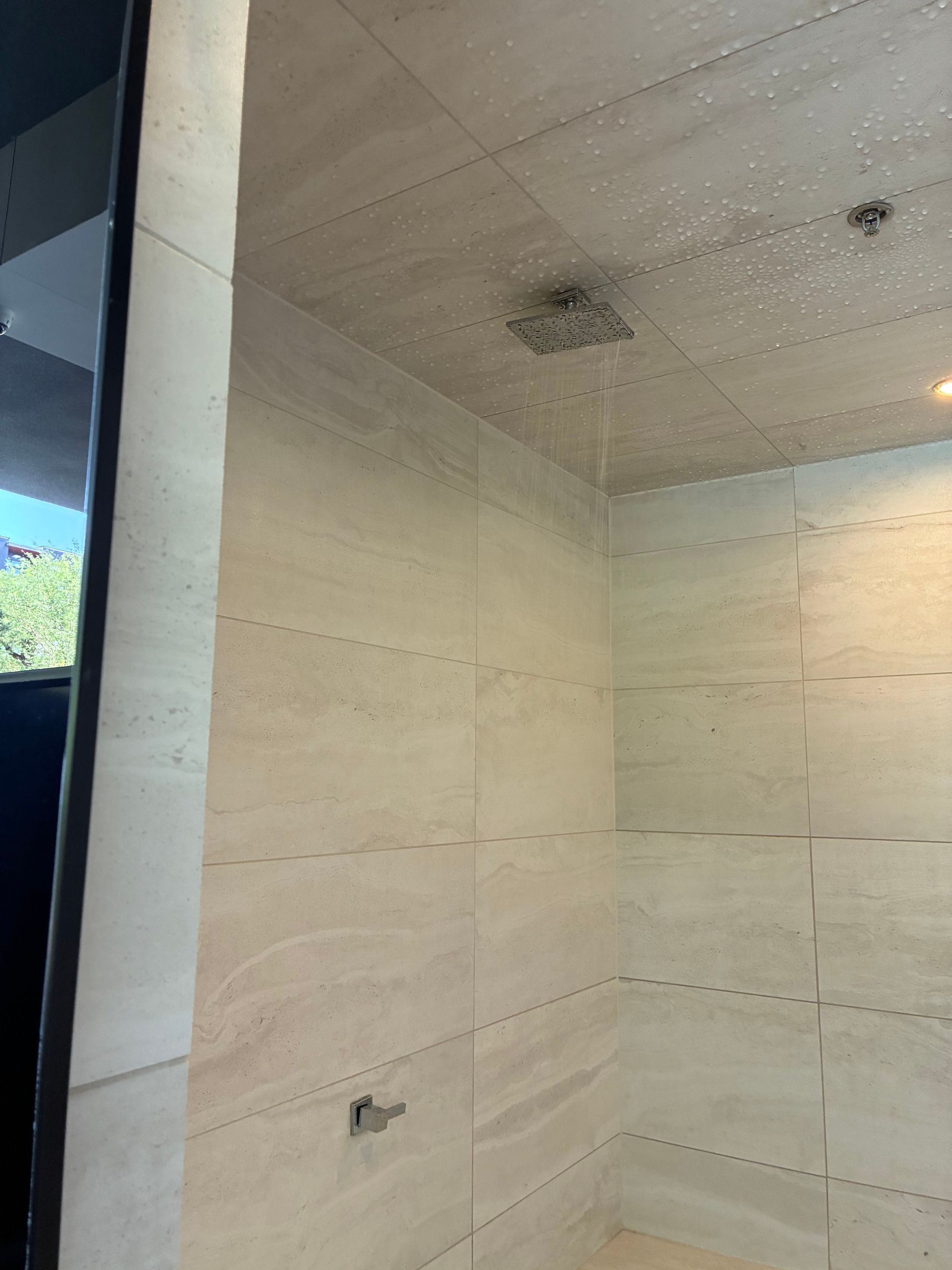 Shower with light beige tiled walls and ceiling. A square shower head is mounted in the ceiling.