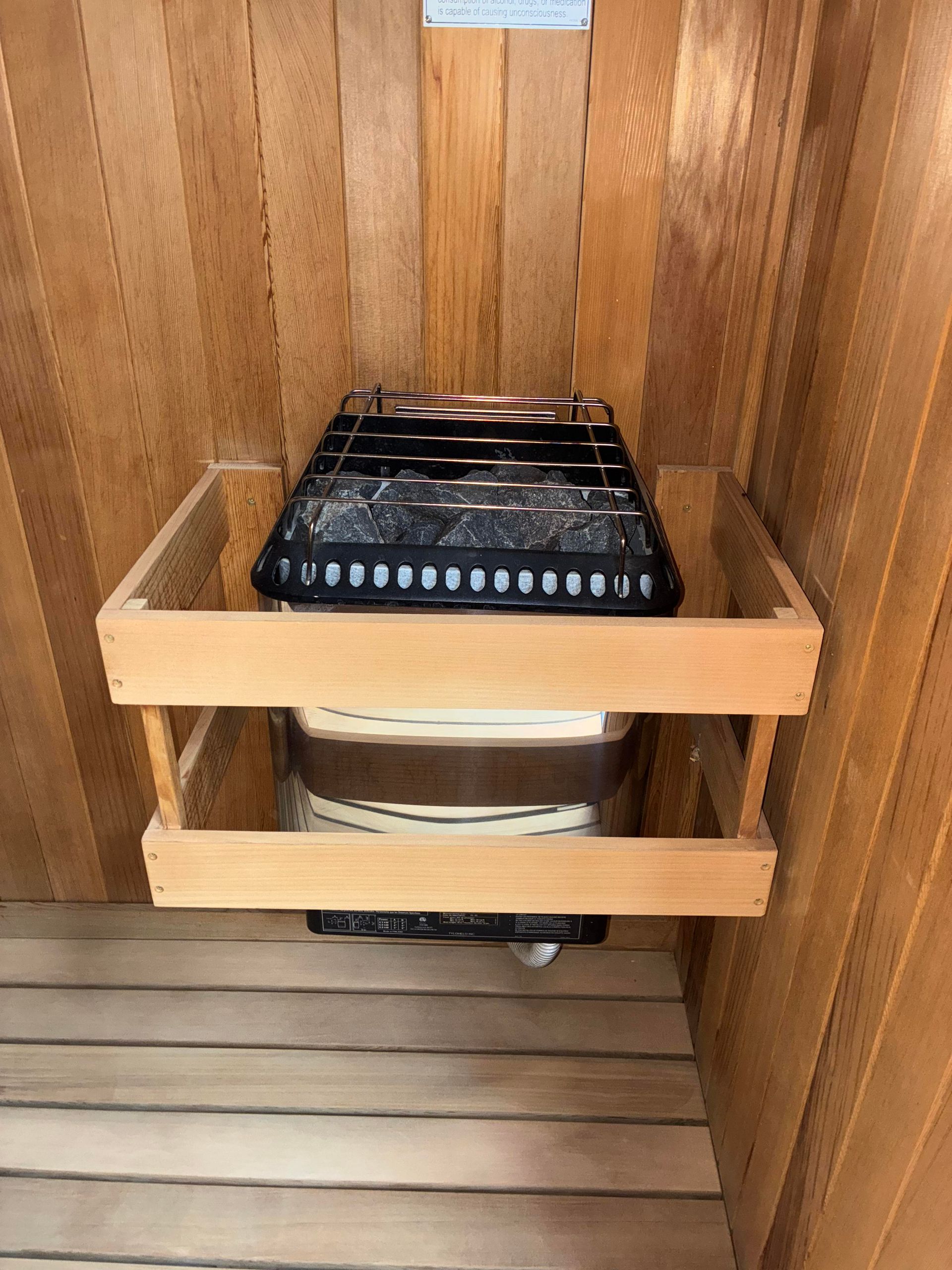 Sauna interior with wooden walls. A heater with rocks is inside a wooden guard.
