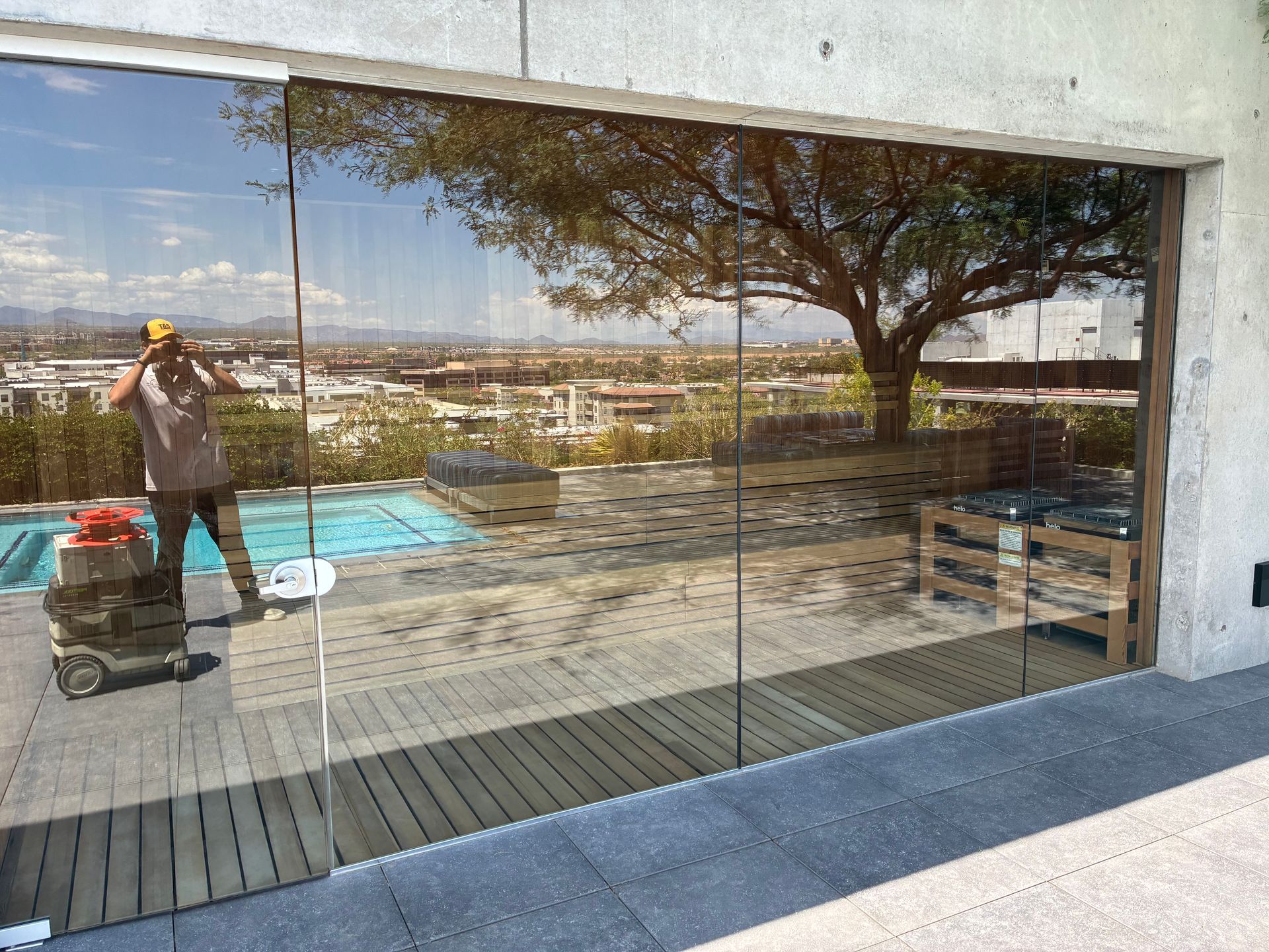 Large glass doors reflect a sunny outdoor scene: a pool, a tree, and a person taking a photo.