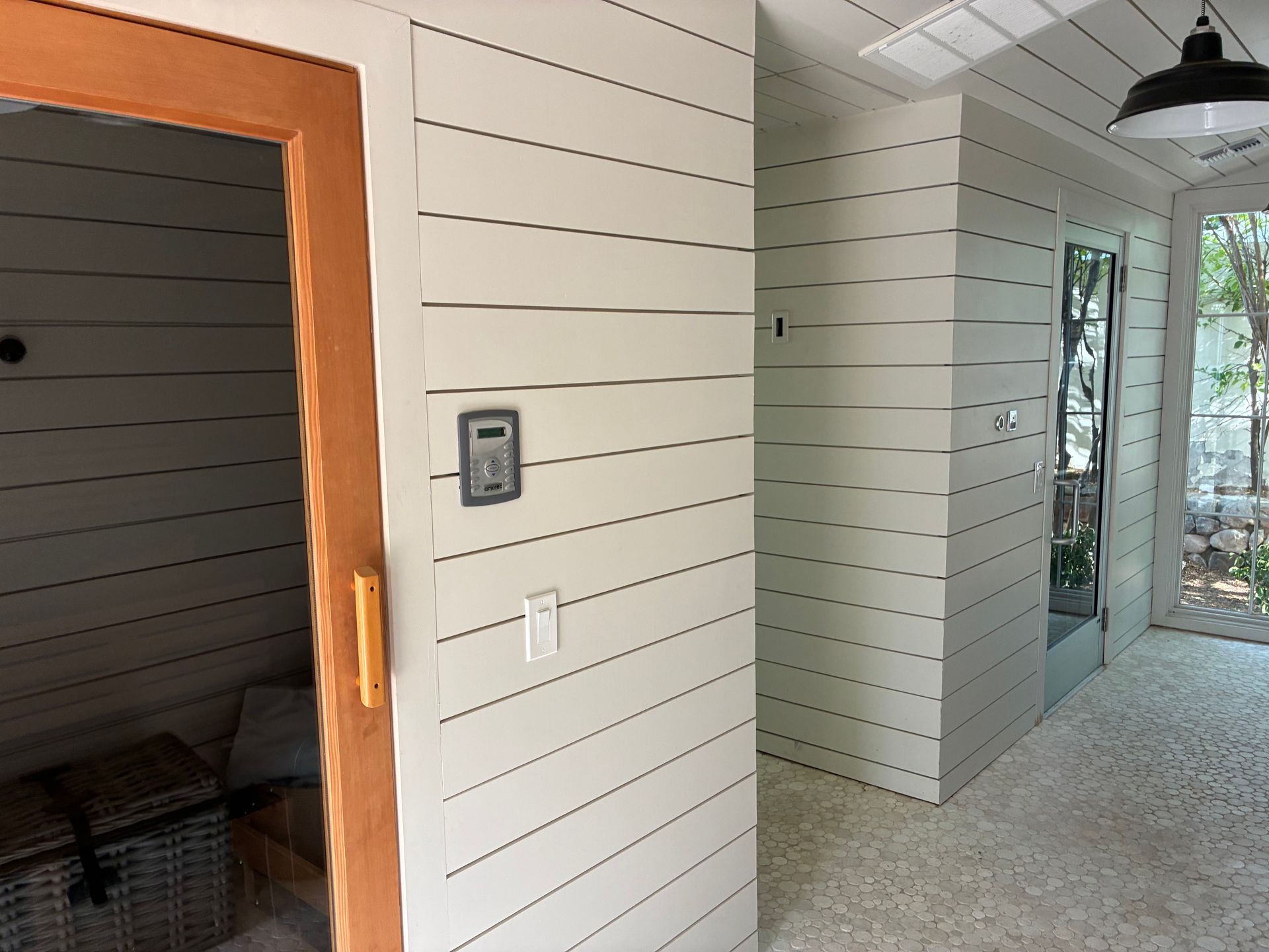 Interior hallway with white horizontal paneling, light flooring, a brown-framed door, and an exterior glass door.