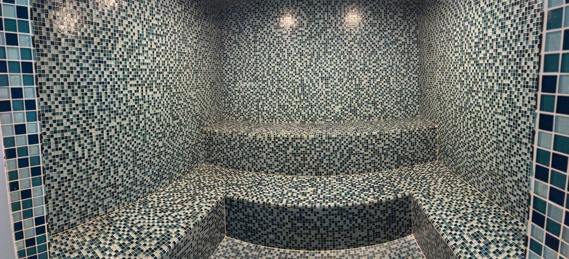 A mosaic-tiled pool with steps and blue accents, illuminated by overhead lights.