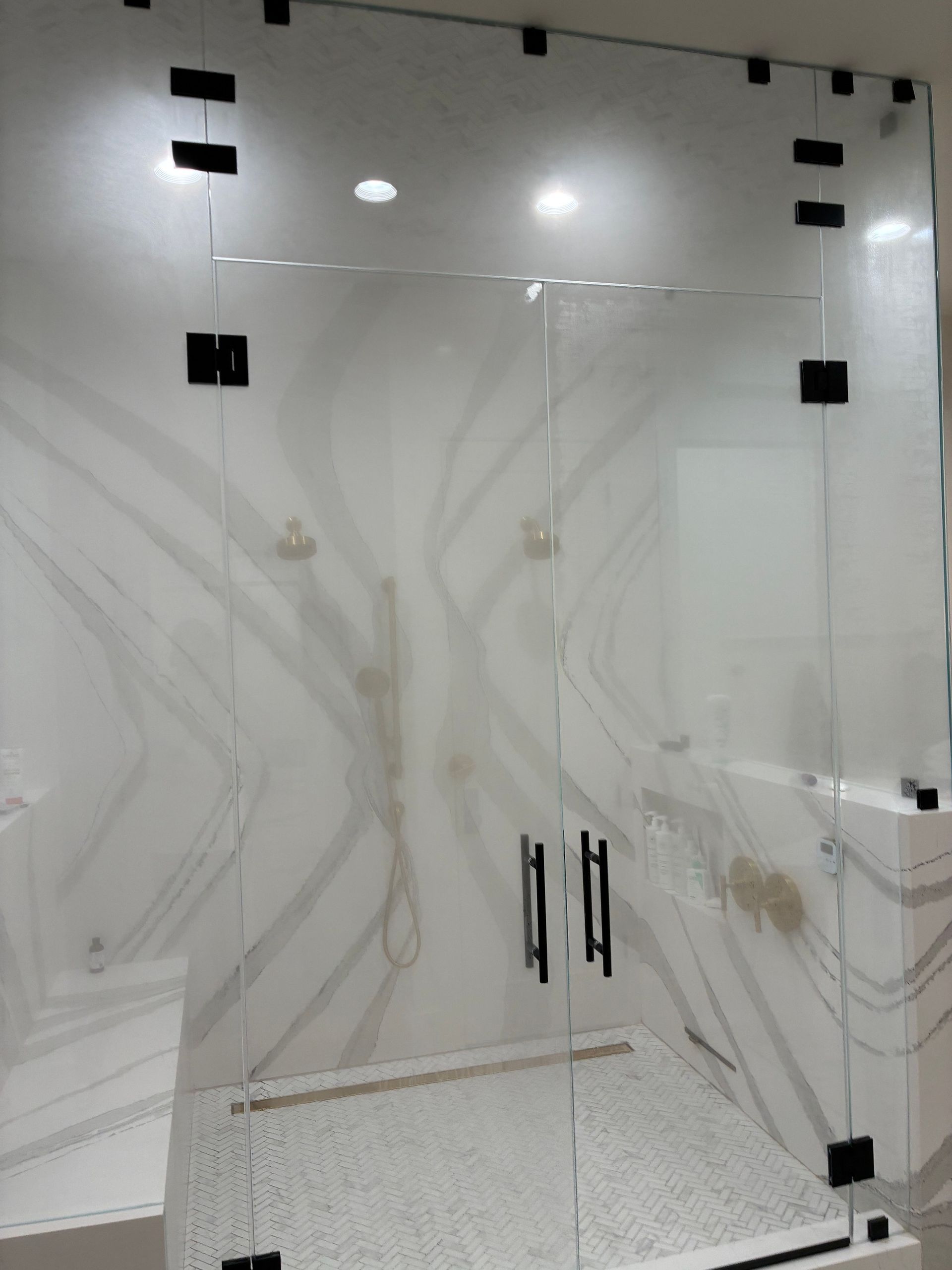 Glass shower enclosure with black hardware against marble-look tile walls.