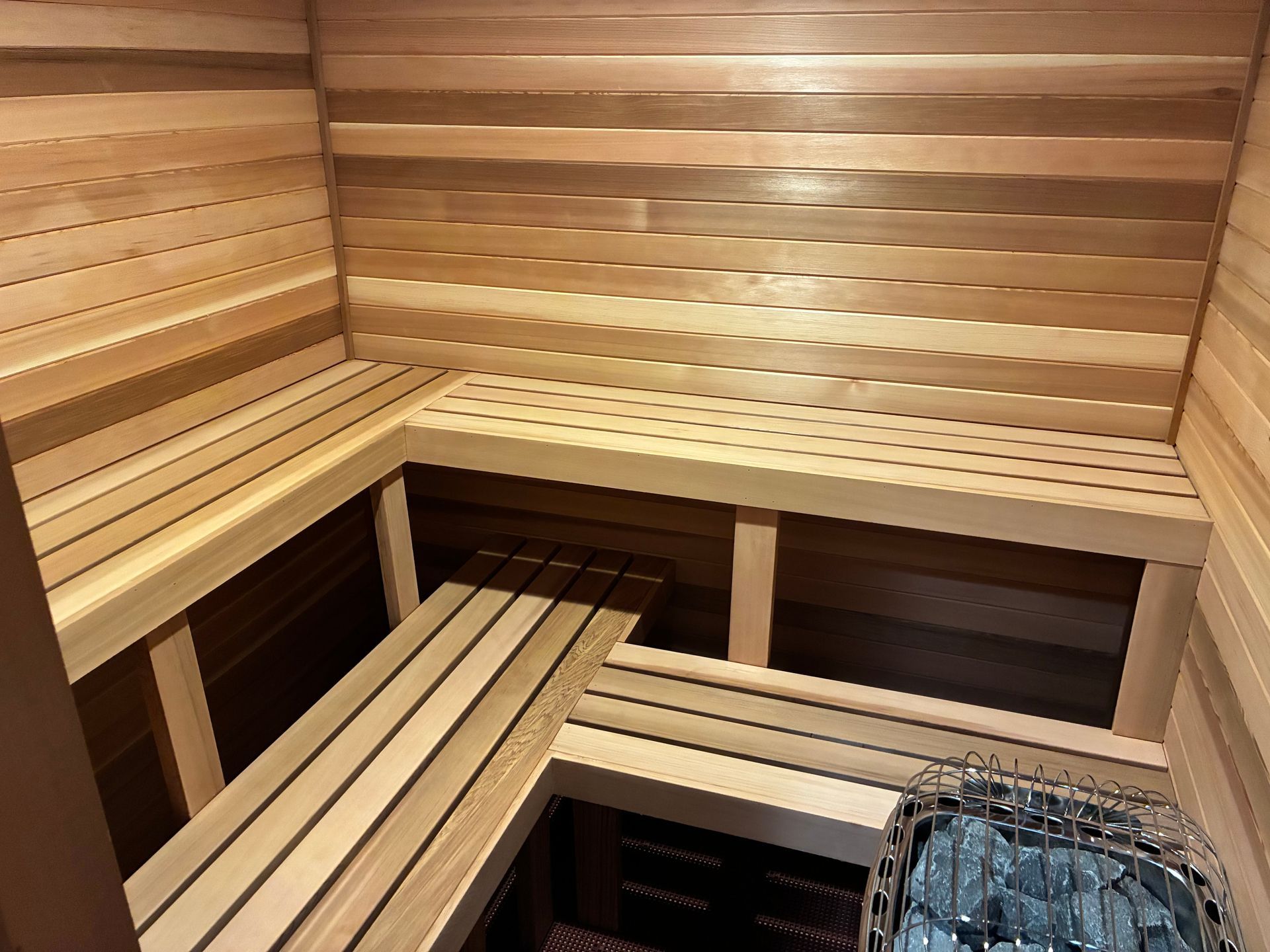 Wooden sauna interior with tiered benches and heating rocks.