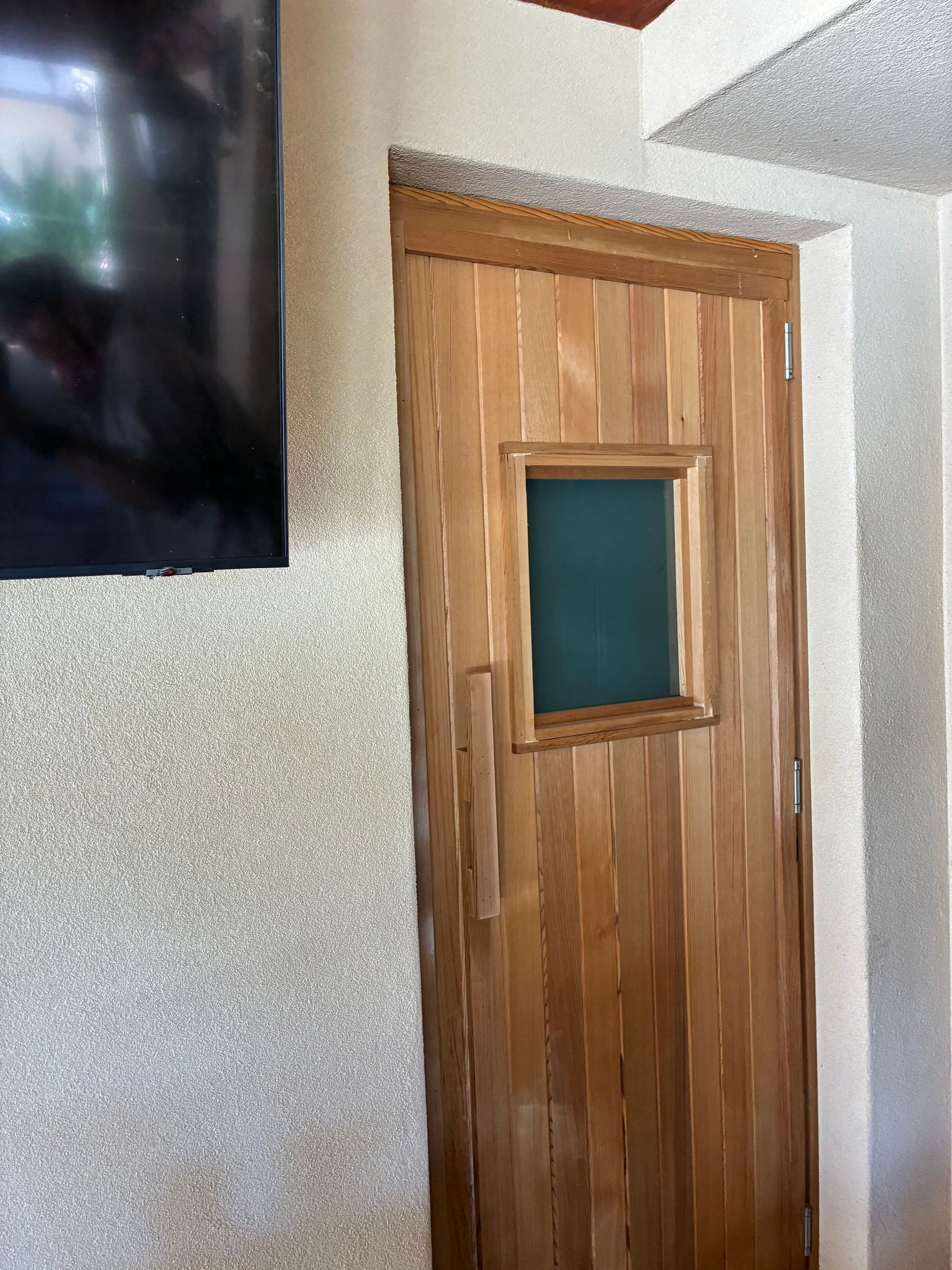 Wooden door with small green window, set in a textured wall.